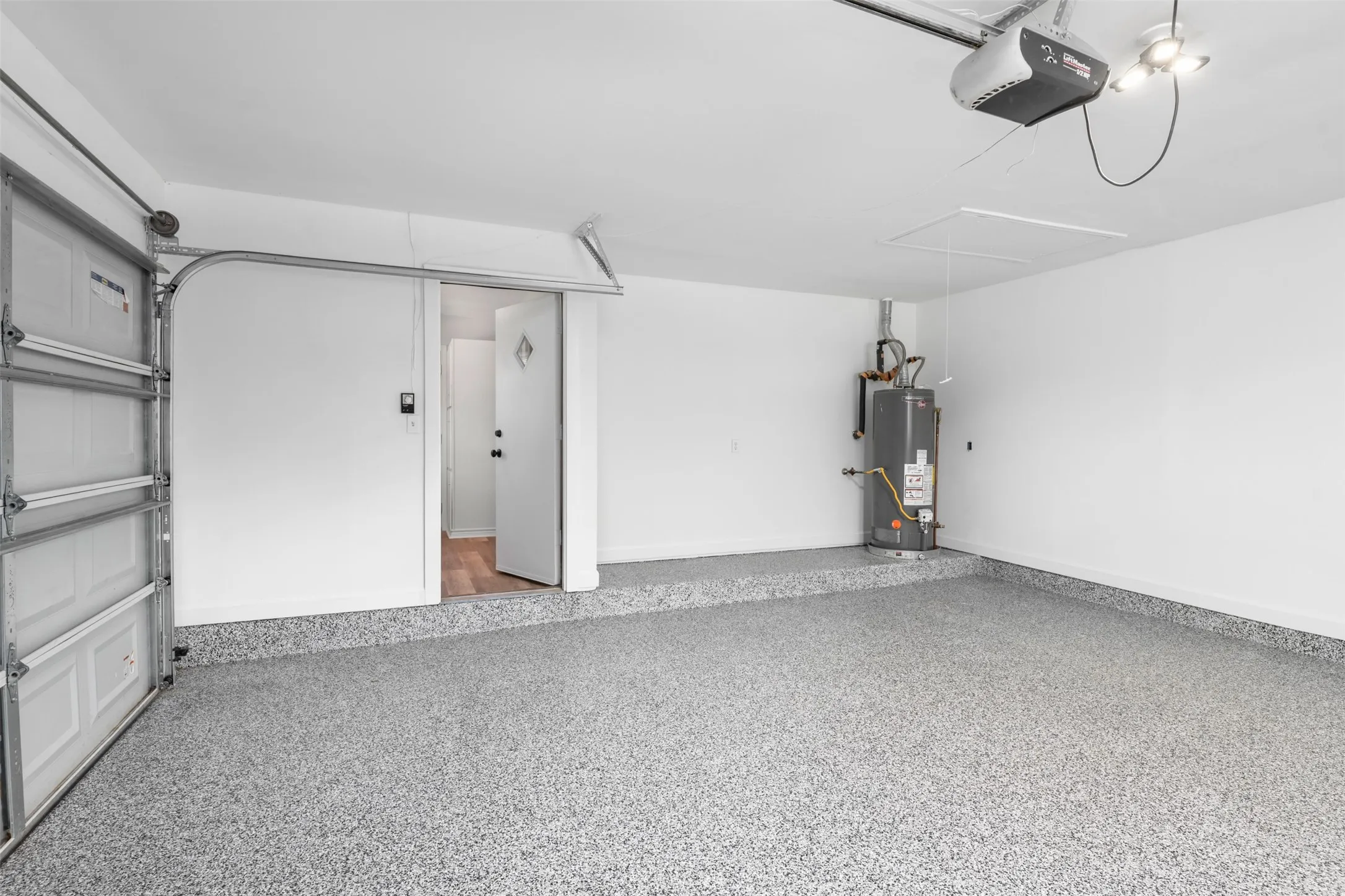 Garage featuring a speckled epoxy floor, white painted walls, and a finished ceiling with overhead lighting