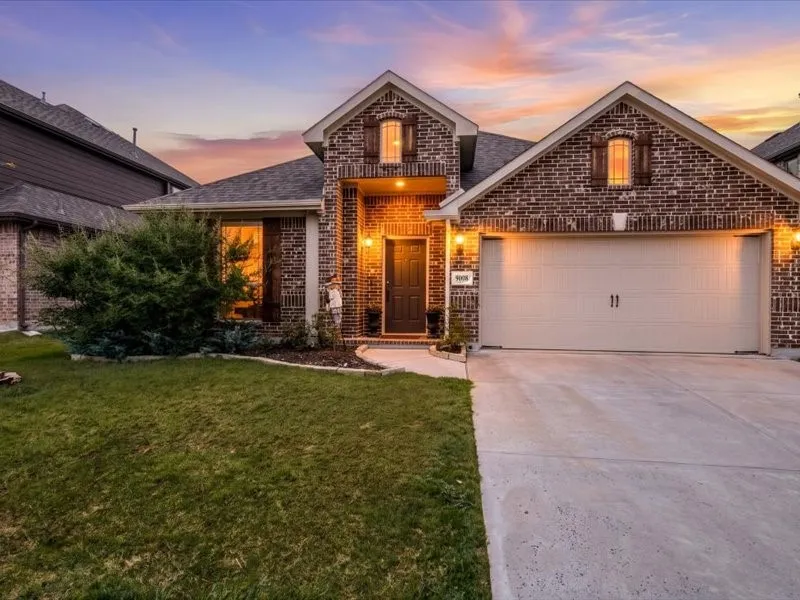 Brick exterior with dark shutters, attached garage, concrete driveway, and front landscaping