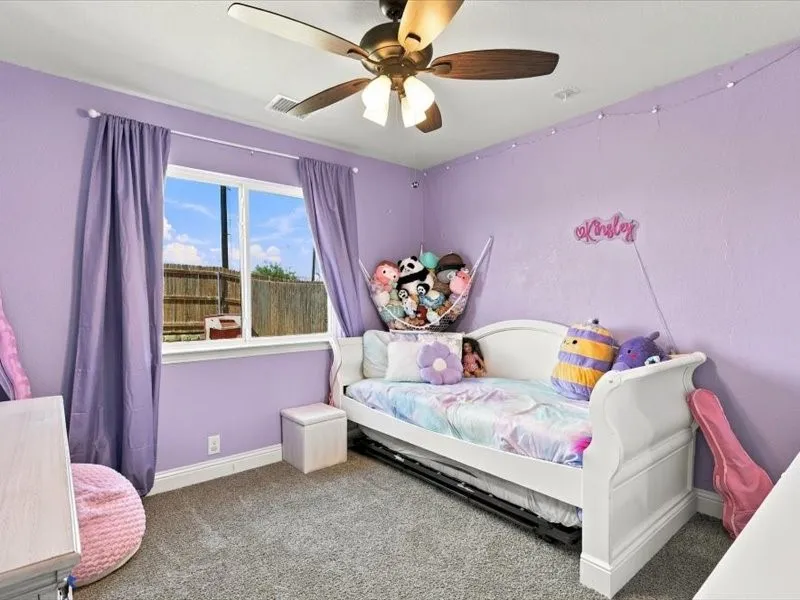 Window with privacy fencing beyond, ceiling fan with light fixture, and wall-to-wall carpeting