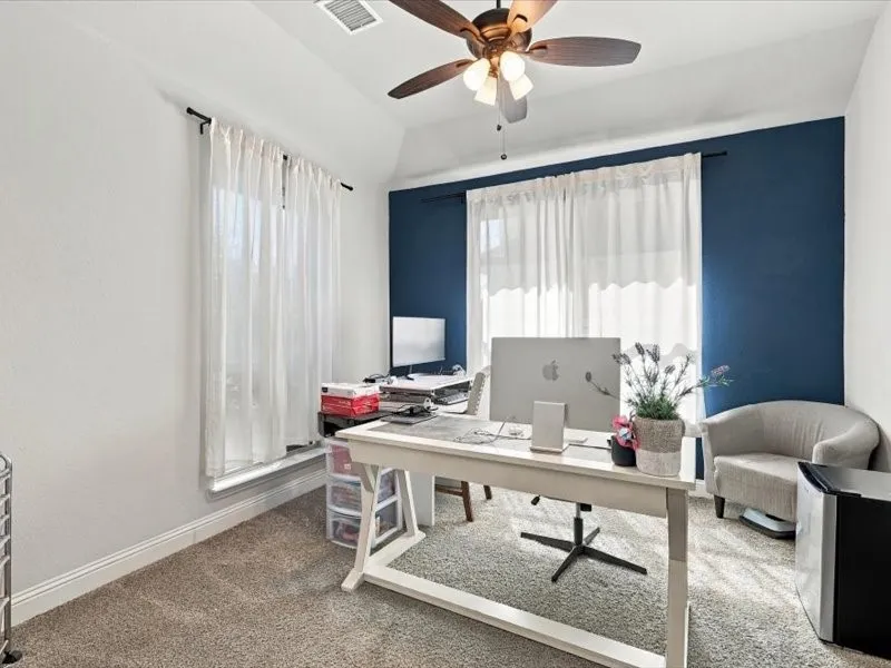 Vaulted ceiling, ceiling fan with light fixture, carpeted flooring, accent wall, and window with white curtains