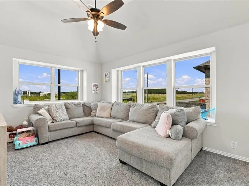 Vaulted ceiling with a ceiling fan, light gray wall paint, light gray carpeting, and multiple windows