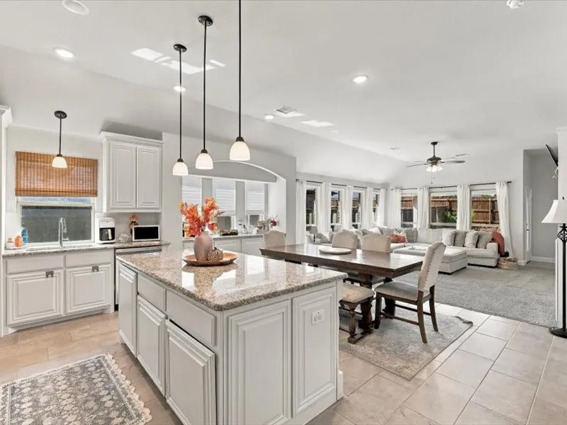 Kitchen island with granite countertop, white cabinetry, and pendant lighting