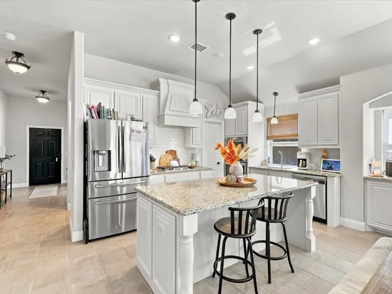 Kitchen featuring a central island with granite countertop, white cabinetry, stainless steel appliances, and pendant lighting