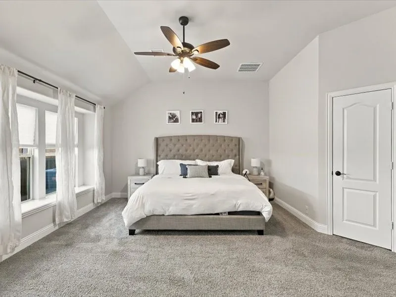 Vaulted ceiling with an attached ceiling fan, dual windows with deep sills, and light gray wall-to-wall carpeting