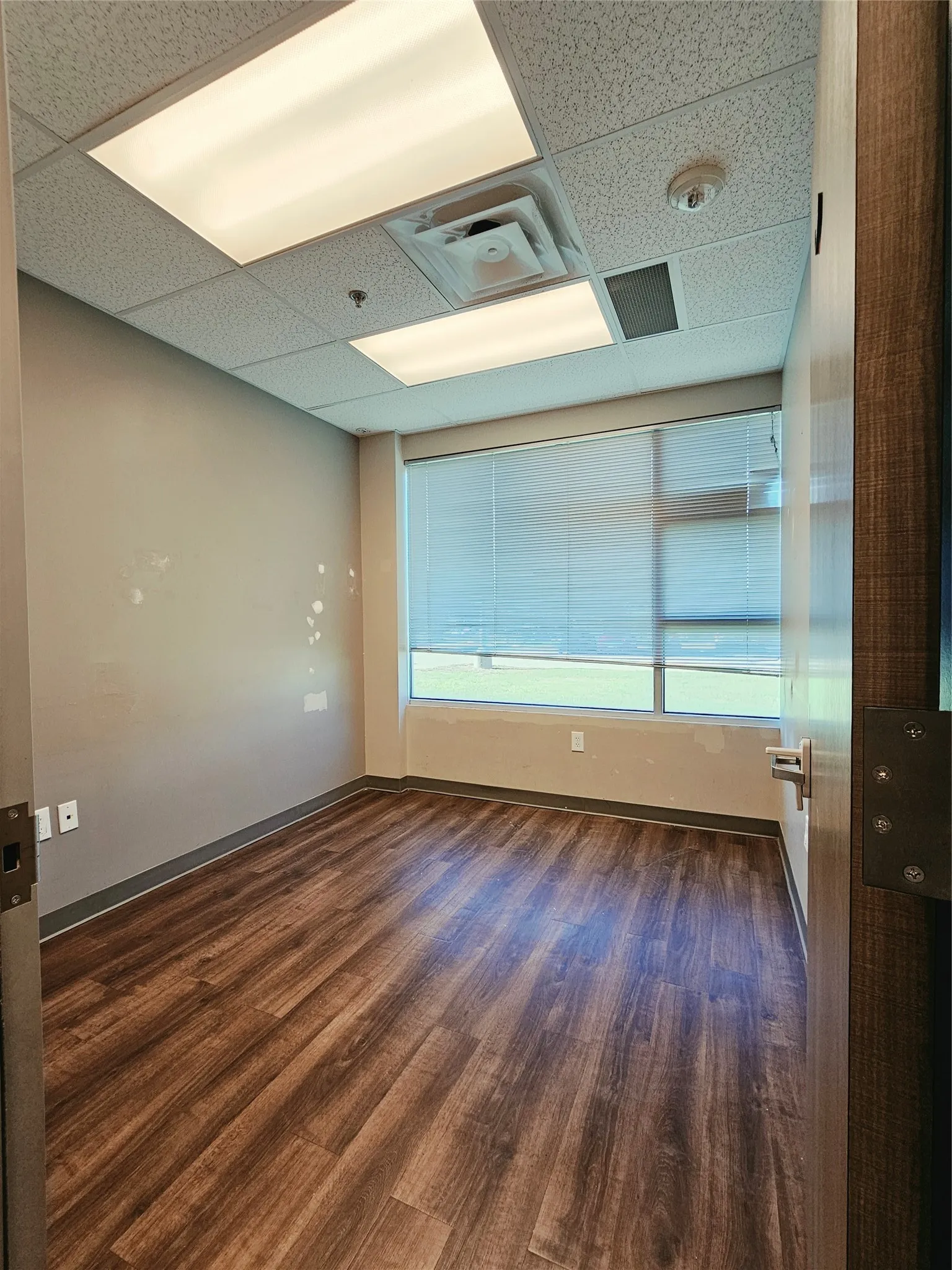 Wood-finish flooring, drop ceiling with integrated lighting, and window with blinds