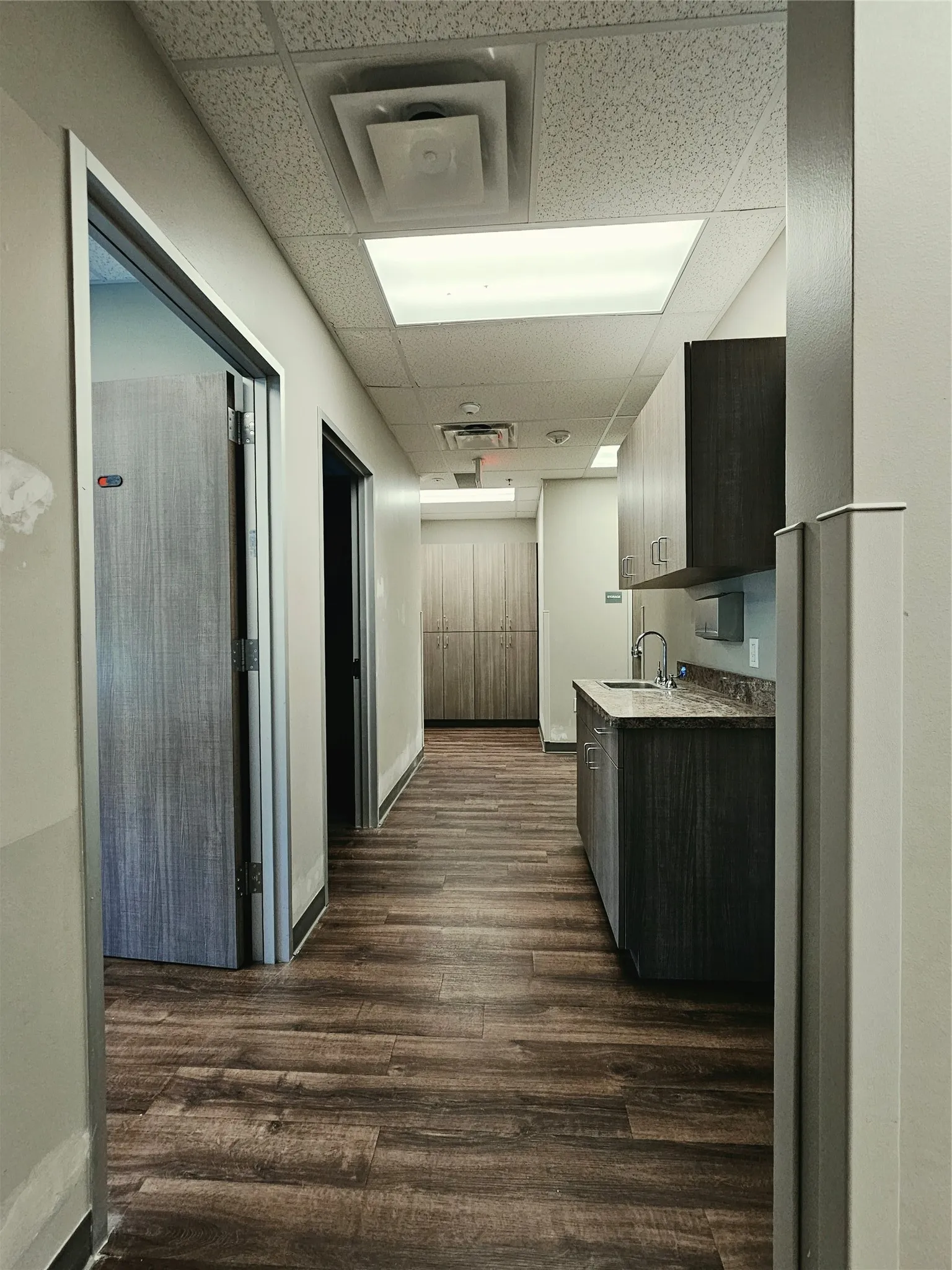 Wood-finish flooring, drop ceiling with recessed lighting, built-in cabinetry, and a countertop with an integrated sink