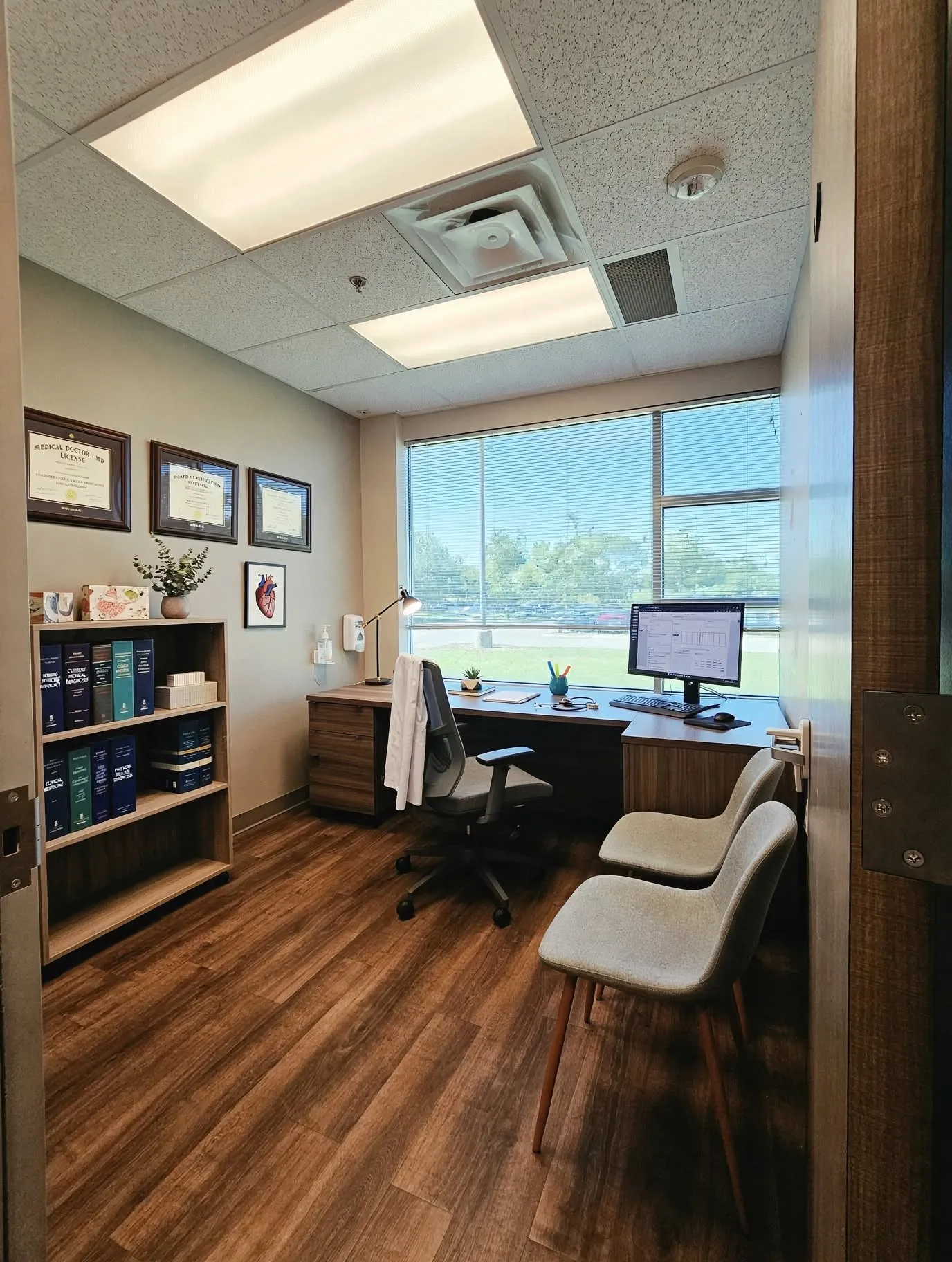 Wood-finish flooring with a built-in desk, shelving unit, and large window with blinds