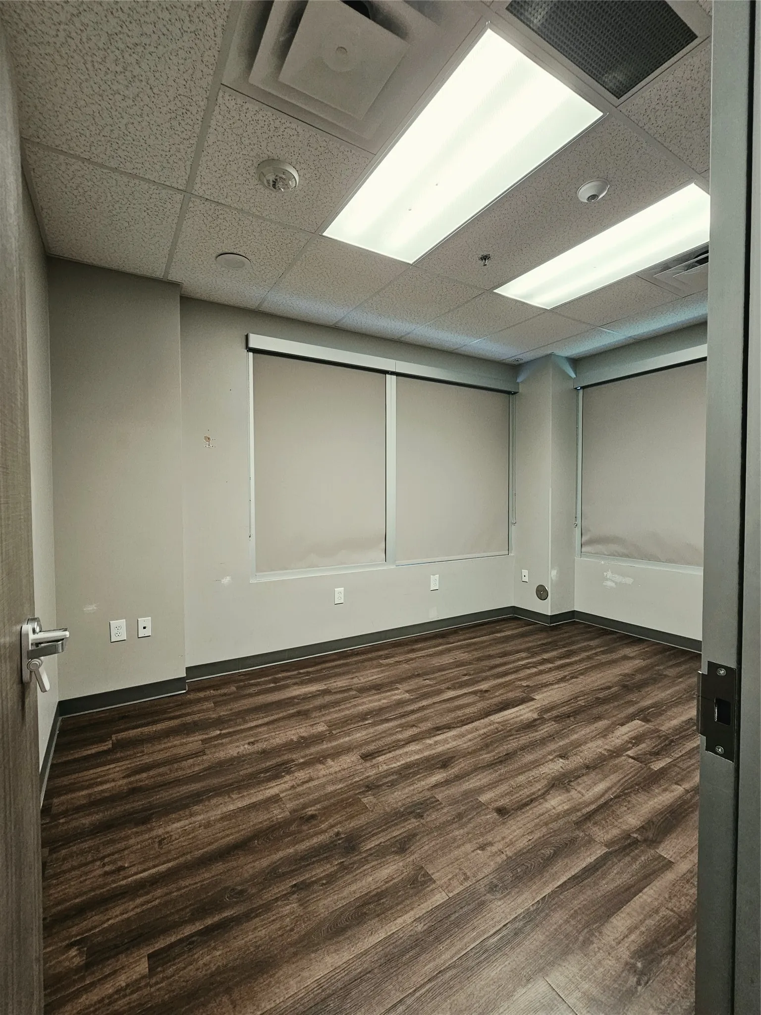 Wood-finish flooring, drop ceiling with integrated lighting, window treatments, and neutral wall tones