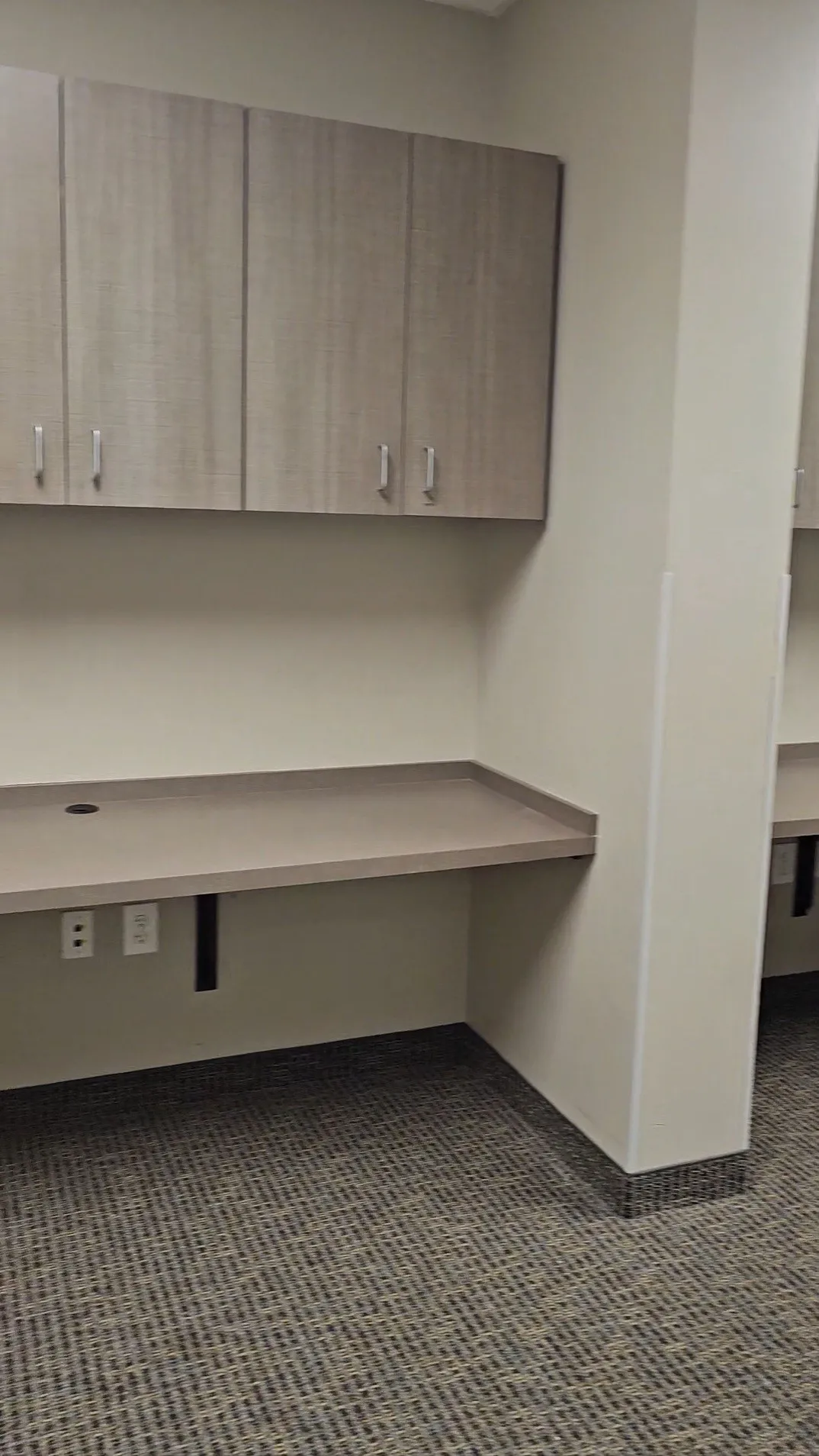 Built-in desk with a smooth surface, integrated power outlets, and overhead cabinetry with contemporary hardware