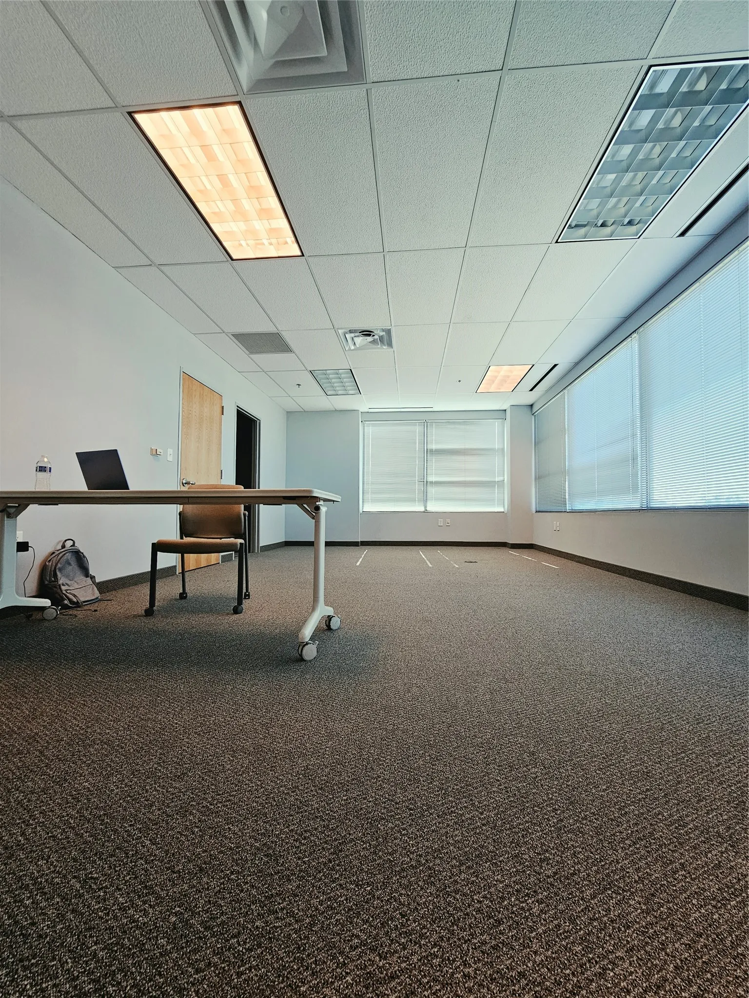 Spacious room featuring textured carpet, multiple windows with blinds, recessed lighting, and a suspended ceiling