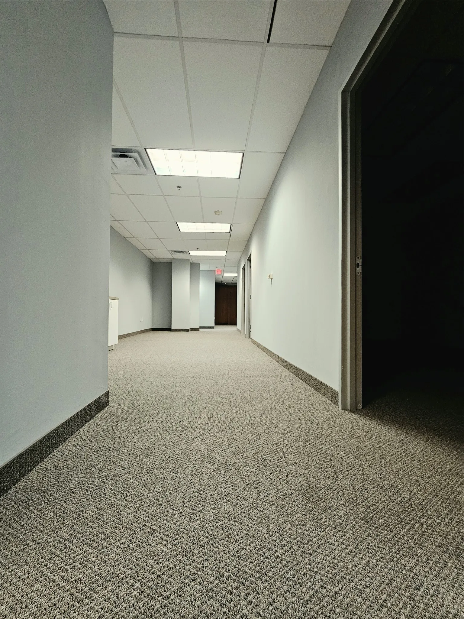 Hallway with commercial-grade carpeting, drop ceiling with integrated lighting, light-toned walls, and dark baseboards
