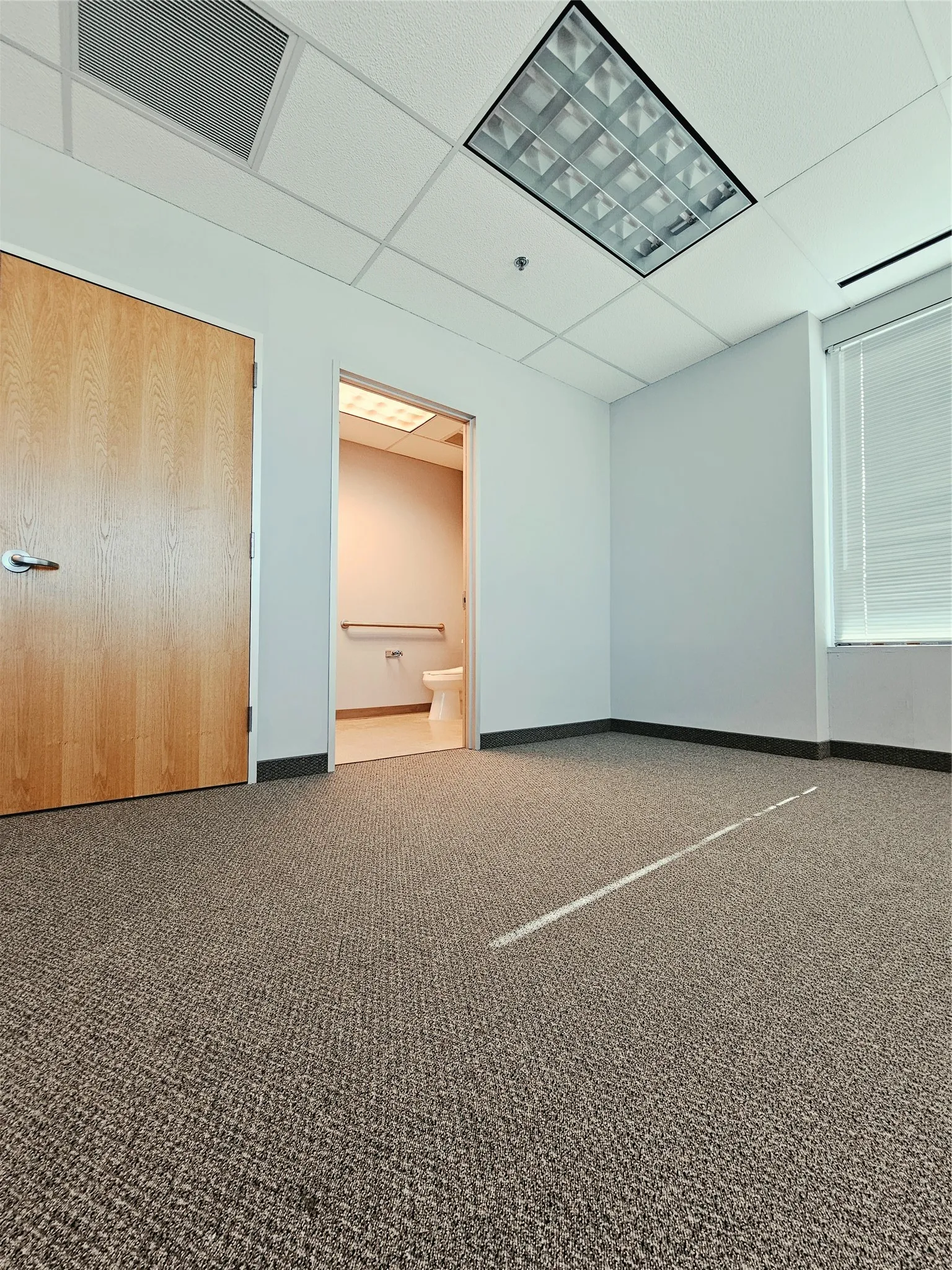 Textured carpet flooring, white walls, and a suspended ceiling with recessed lighting
