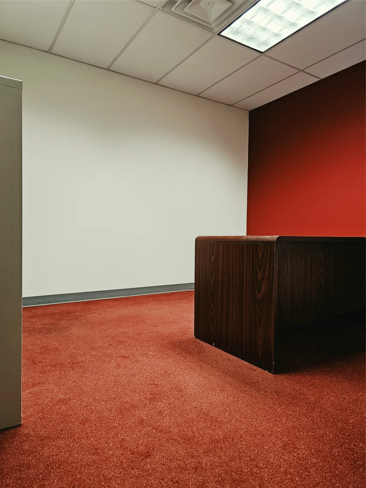Red carpeting, white and accent red walls, wood-finish desk, and drop ceiling with recessed lighting
