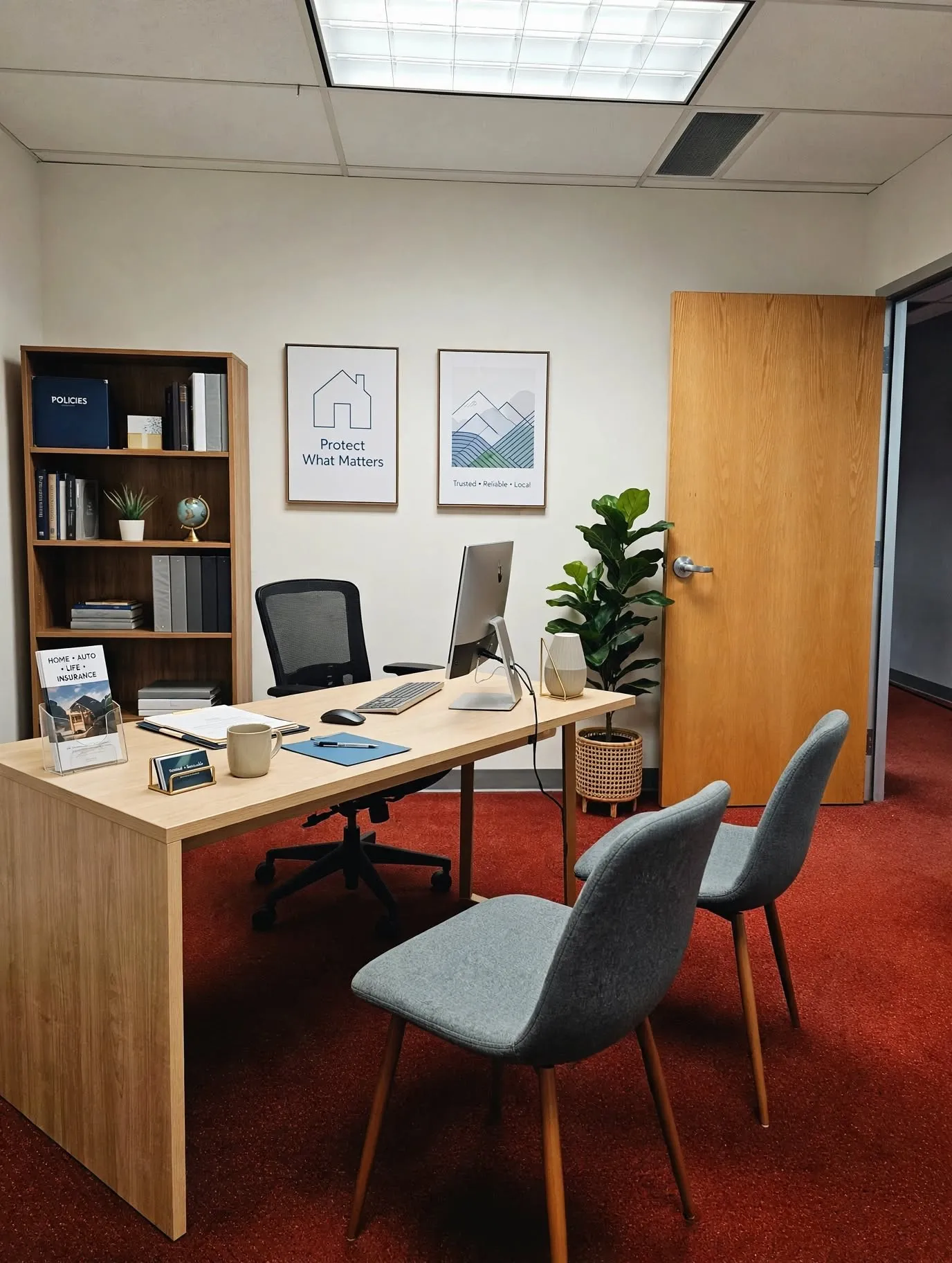 Light wood-finish desk with integrated modesty panel, red textured carpeting, and a built-in wood-finish bookcase