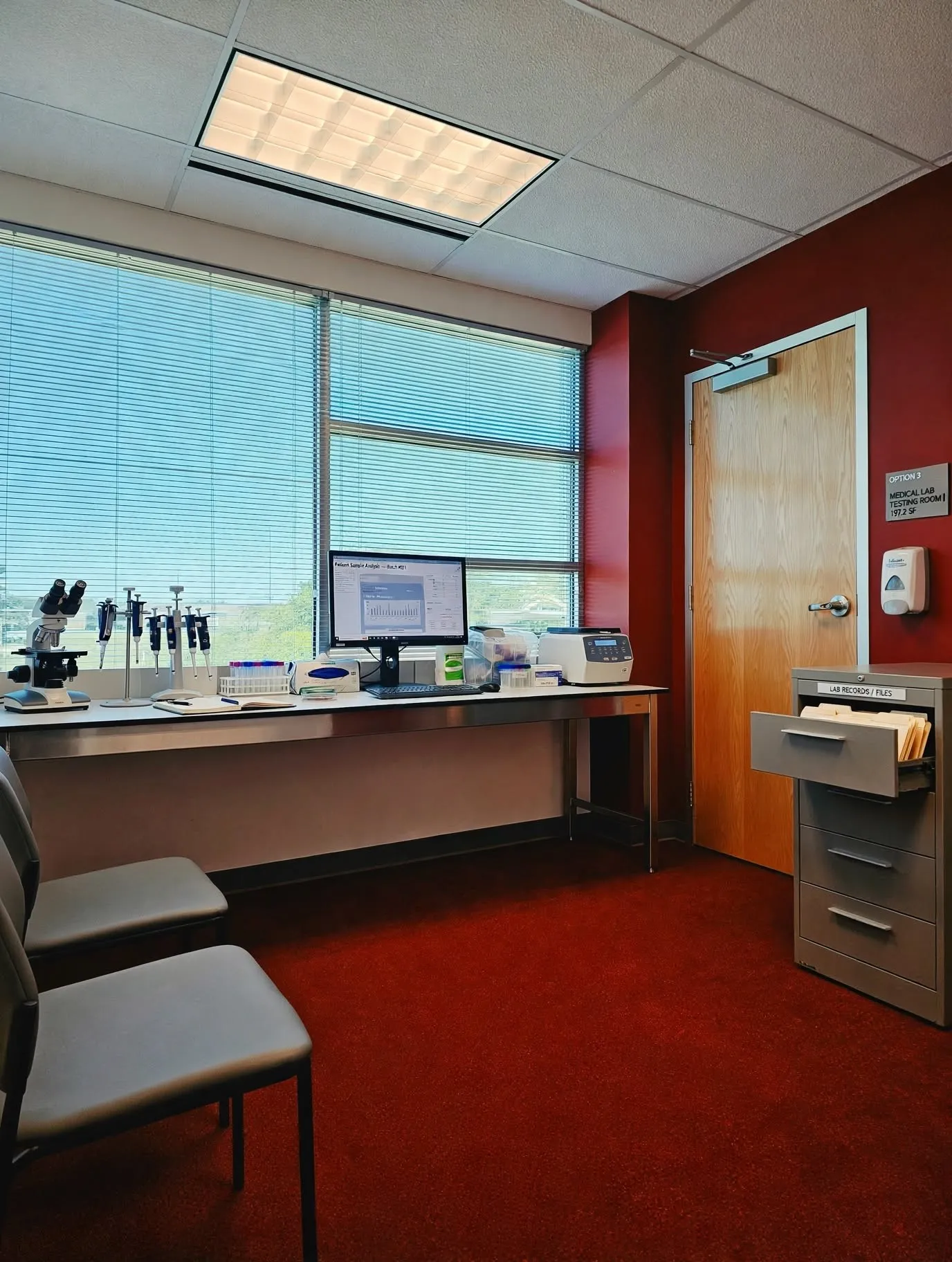 Recessed ceiling lighting, large windows with horizontal blinds, red wall finish, wood-finish door, and red carpet flooring