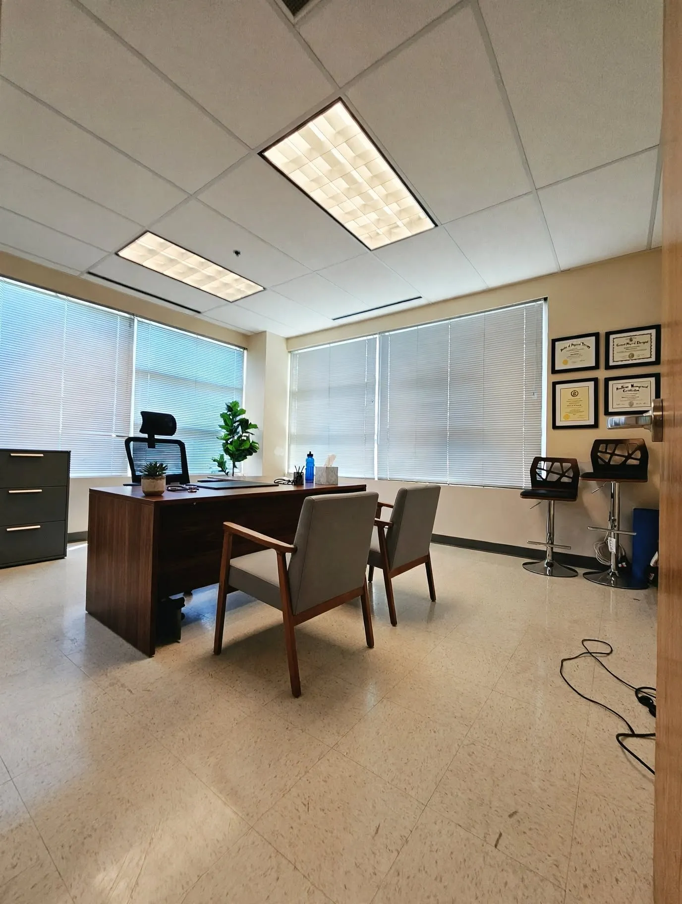 Recessed fluorescent lighting, large windows with horizontal blinds, light-toned flooring, and a solid-core door