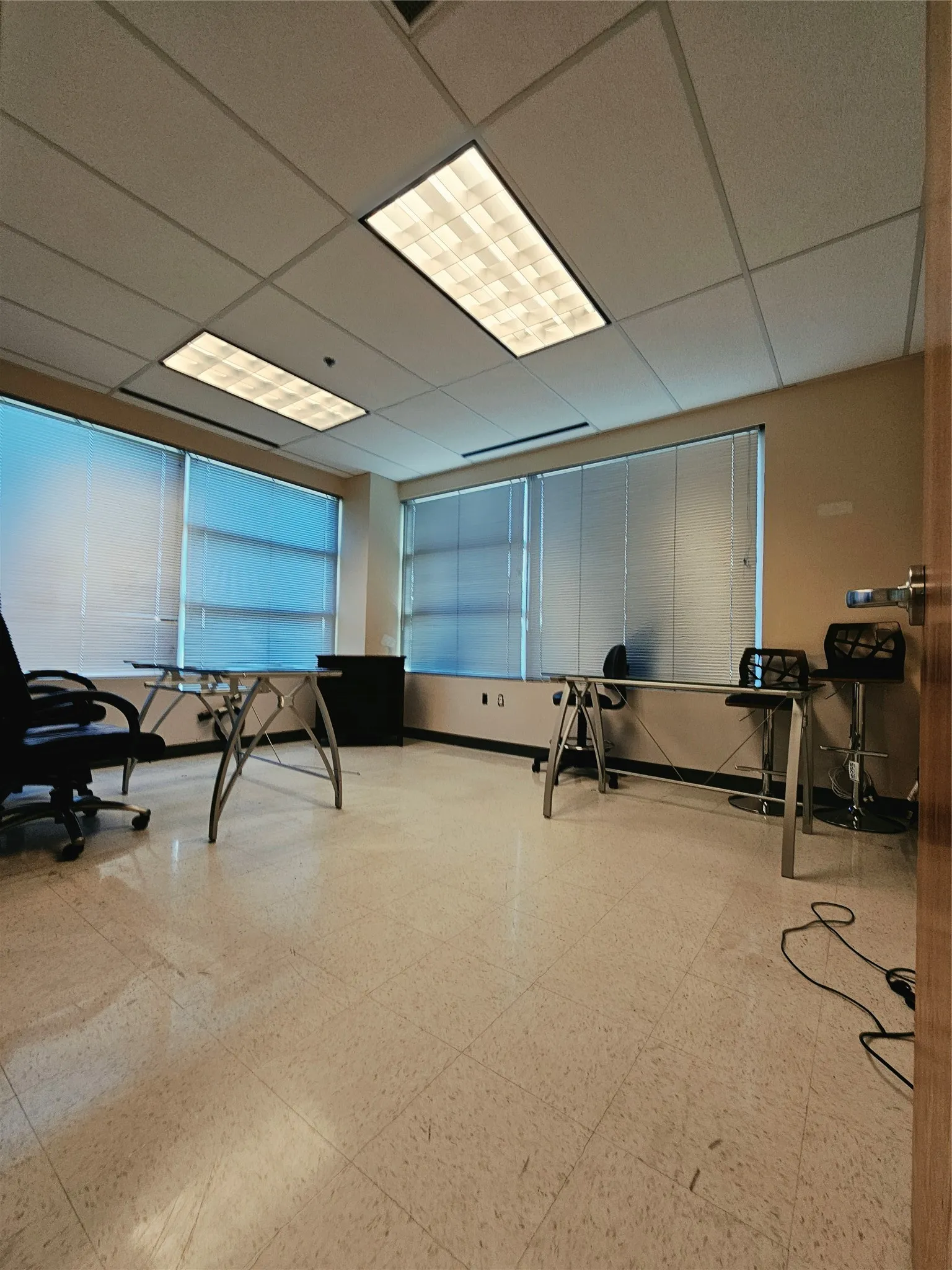 Fluorescent overhead lighting, drop ceiling, multiple windows with horizontal blinds, light-toned tile flooring, and neutral wall paint
