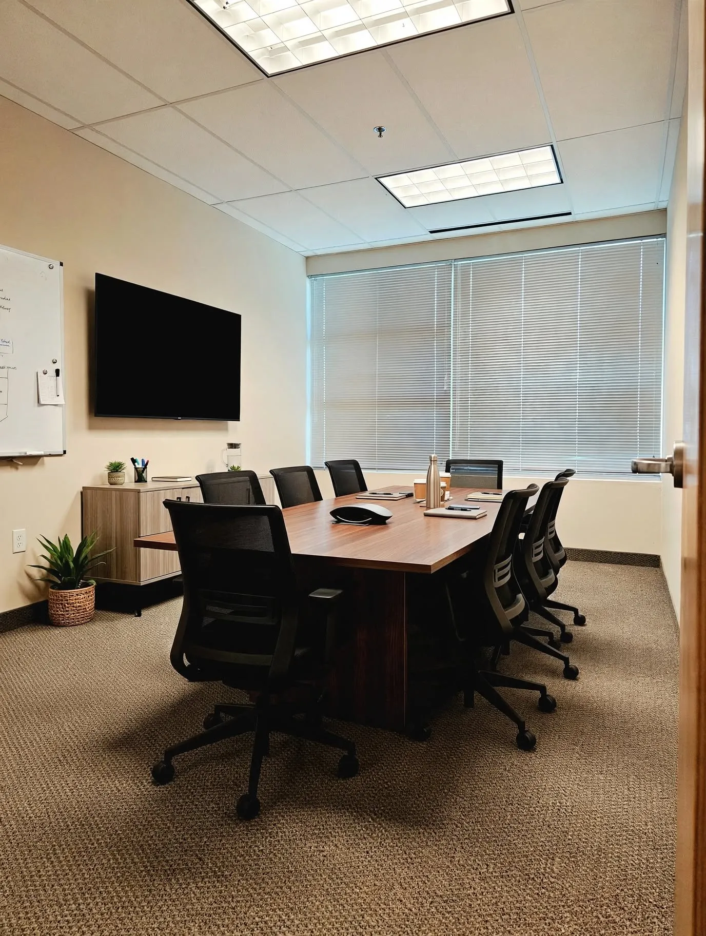 Recessed lighting, wood-finish conference table, textured carpeting, large wall-mounted display, and horizontal window​​‌​​​​‌​​‌‌​‌‌​​​‌‌​‌​‌​‌​​​‌​​ blinds