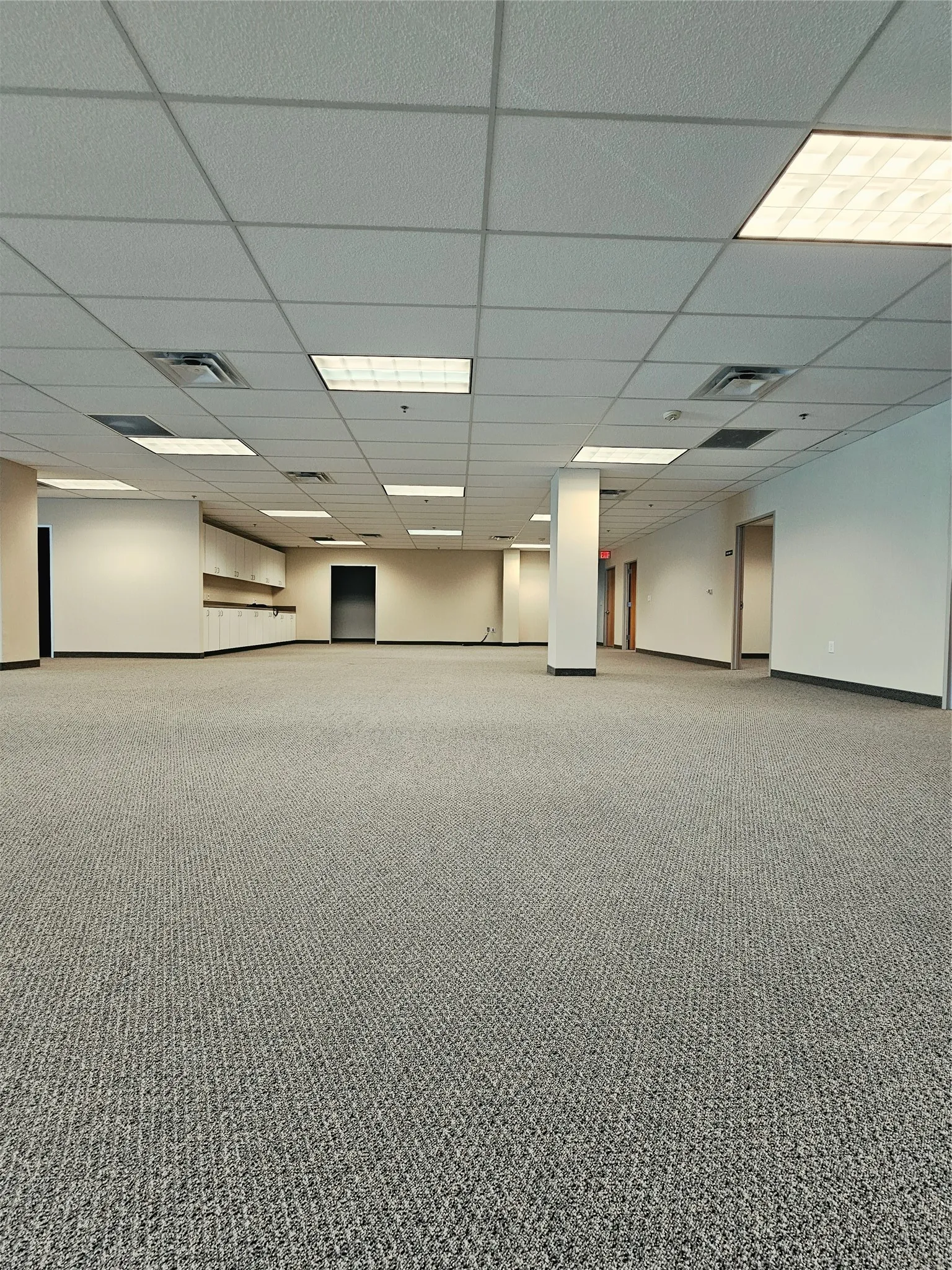 Expansive open-plan area featuring textured carpet flooring, suspended acoustic tile ceiling, and recessed fluorescent lighting