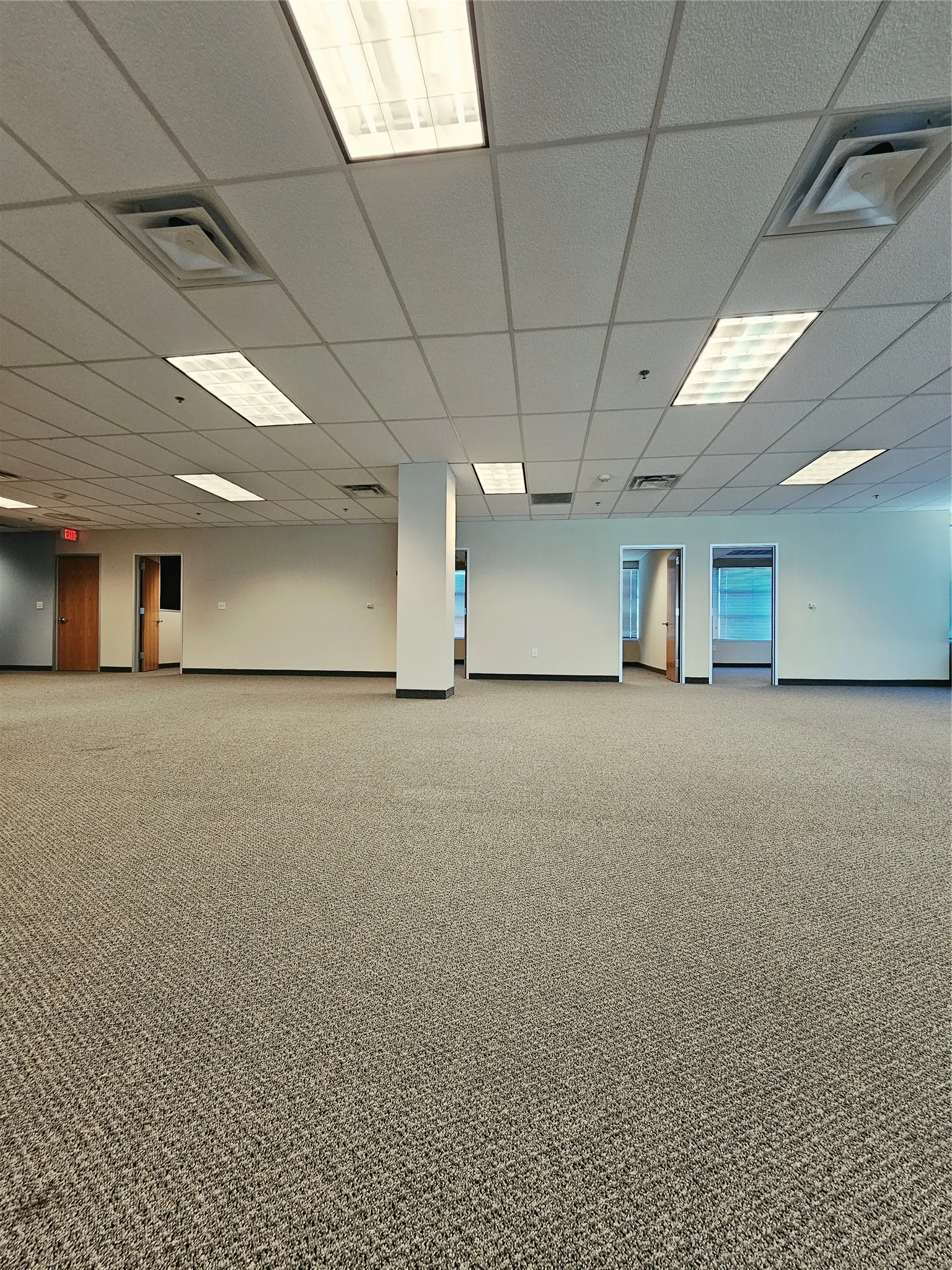 Expansive open-plan interior featuring neutral-toned carpeting and a grid ceiling with recessed lighting