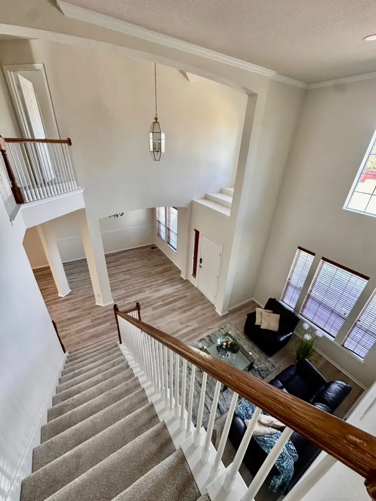 Two-story foyer featuring high ceilings, wood-finish flooring, a hanging pendant light, and a staircase with a wooden handrail and white balusters