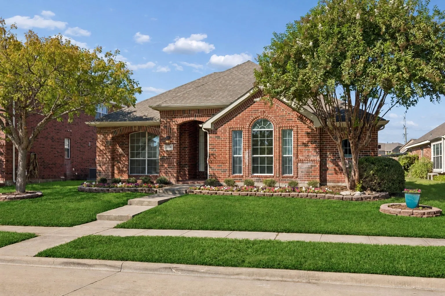 The gorgeous brick archways and charming architectural accents complement the lush, colorful flower beds surrounding the inviting front entrance.