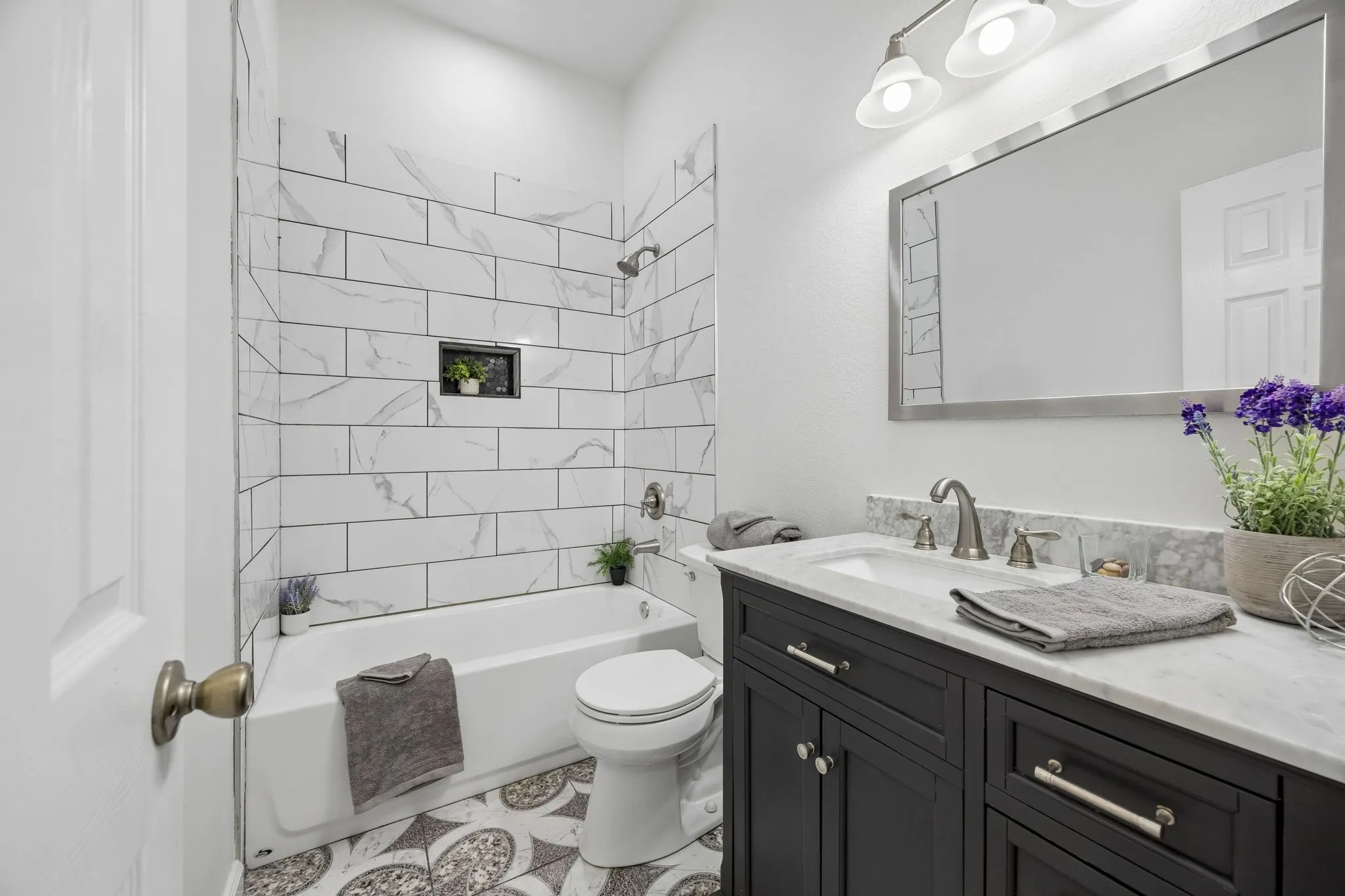 This Guest bath enjoys a combination of sophisticated cabinetry, elegant mirror and lighting, and a relaxing tub-shower combination.