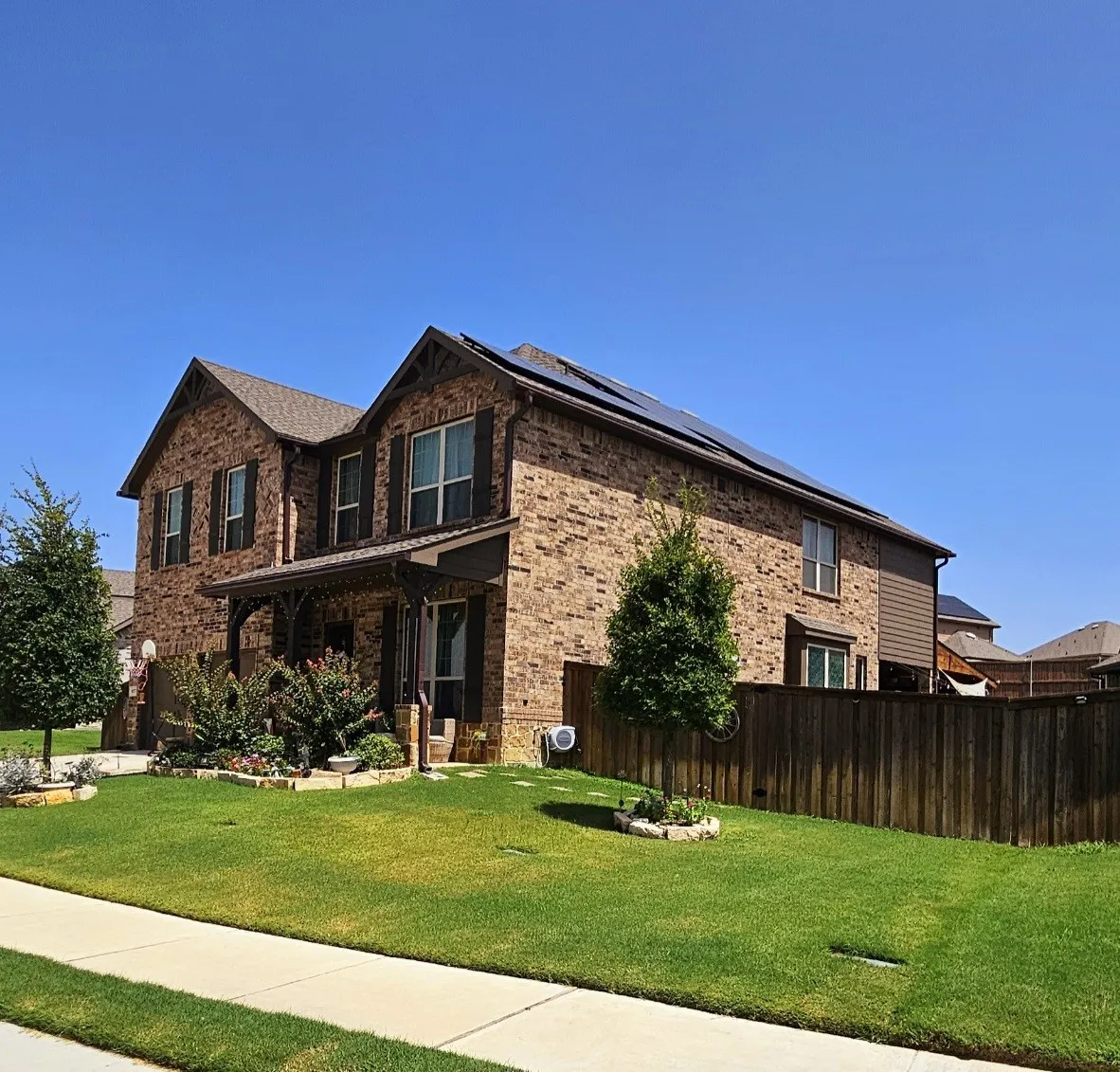 Brick exterior with dark wood shutters, covered front porch, solar panel installation, and a fenced side yard