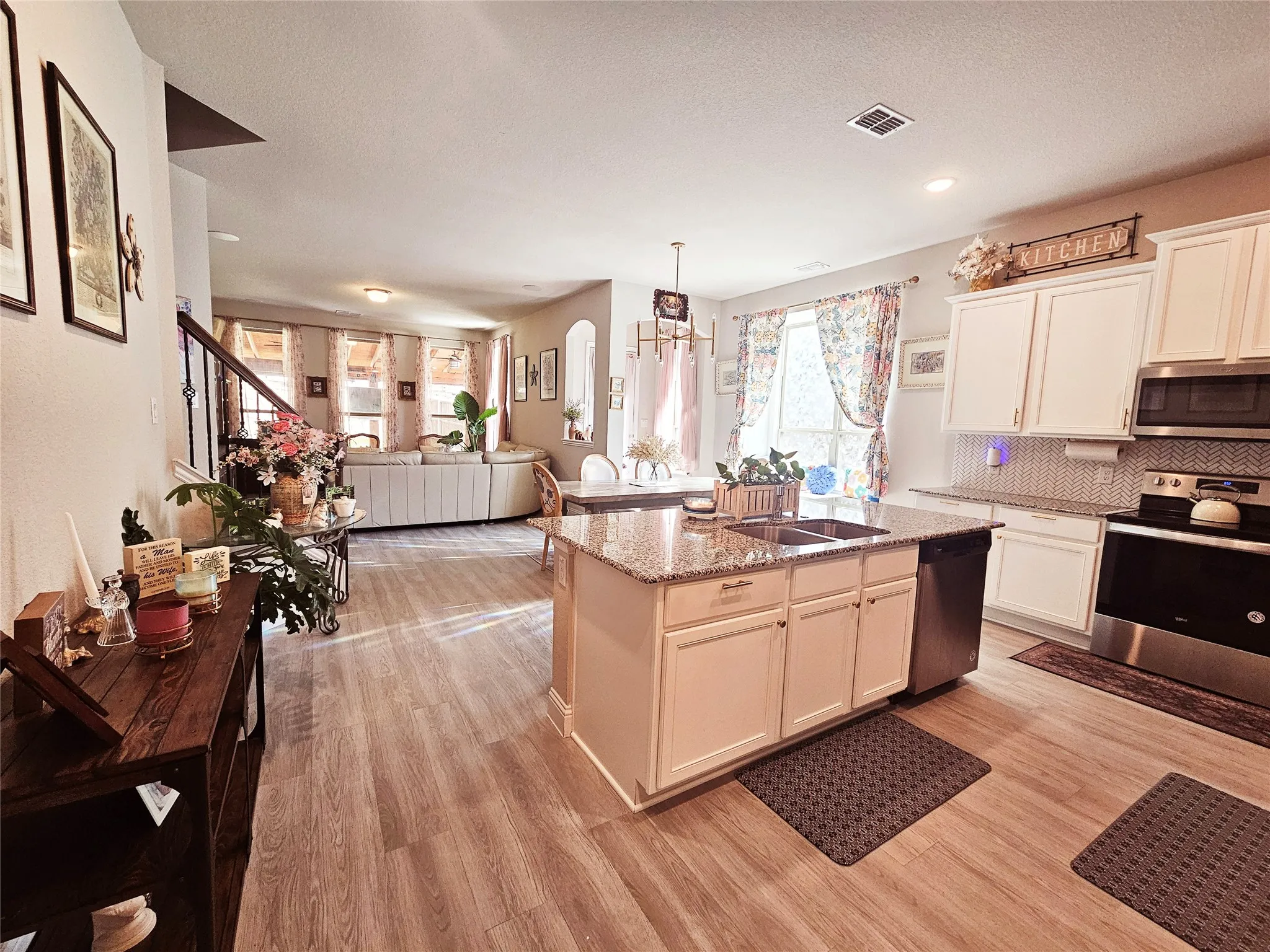 Wood-finish flooring throughout, kitchen island with granite countertop and double-basin sink, white cabinetry with integrated appliances, and a tile backsplash