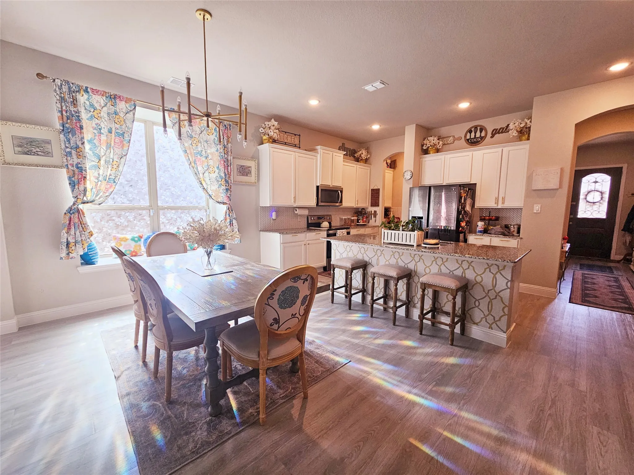 Open-concept kitchen and dining area featuring wood-finish flooring, white cabinetry, recessed lighting, and a kitchen island with seating
