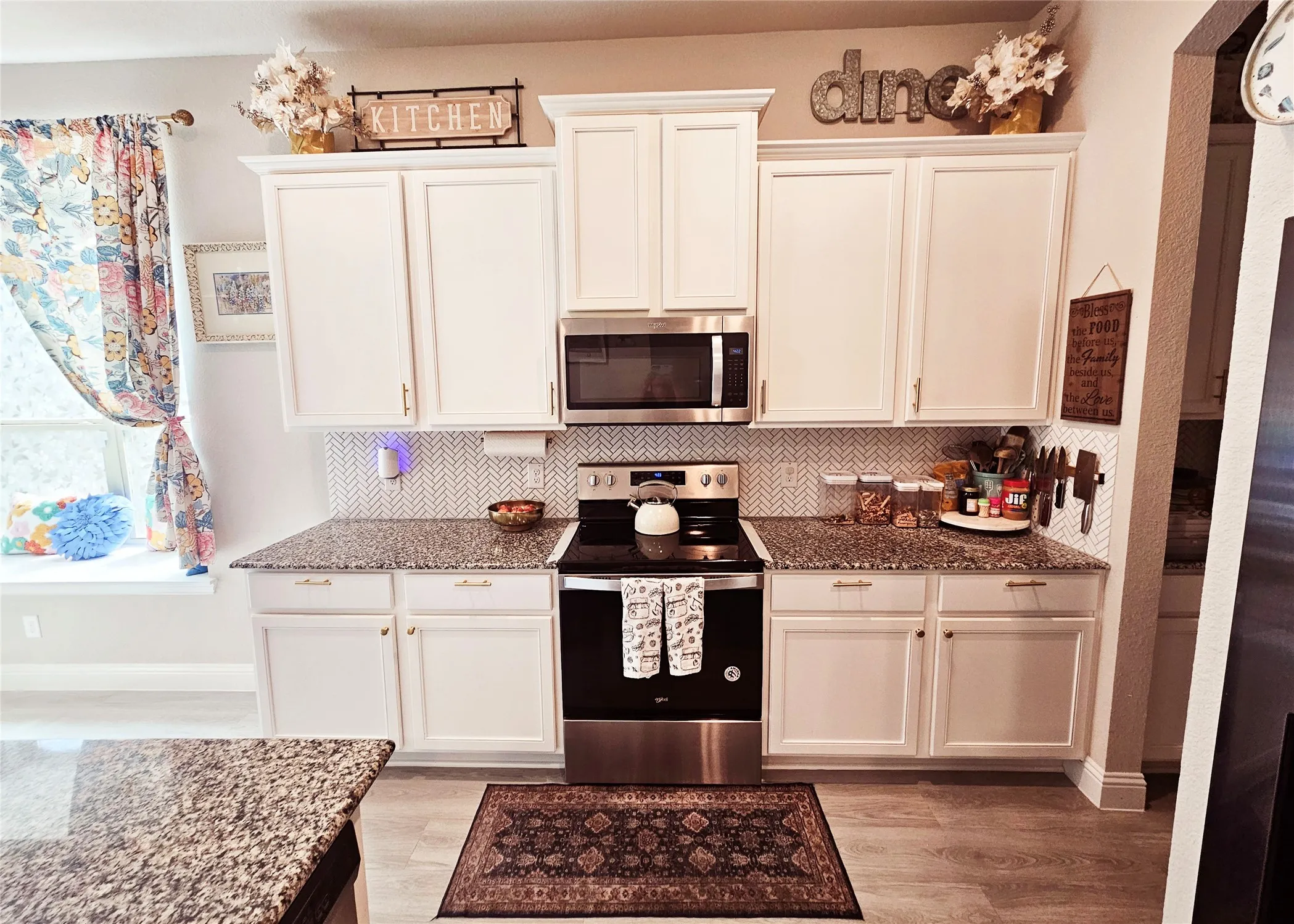 White cabinetry, granite countertops, herringbone tile backsplash, stainless steel appliances, and wood-finish flooring