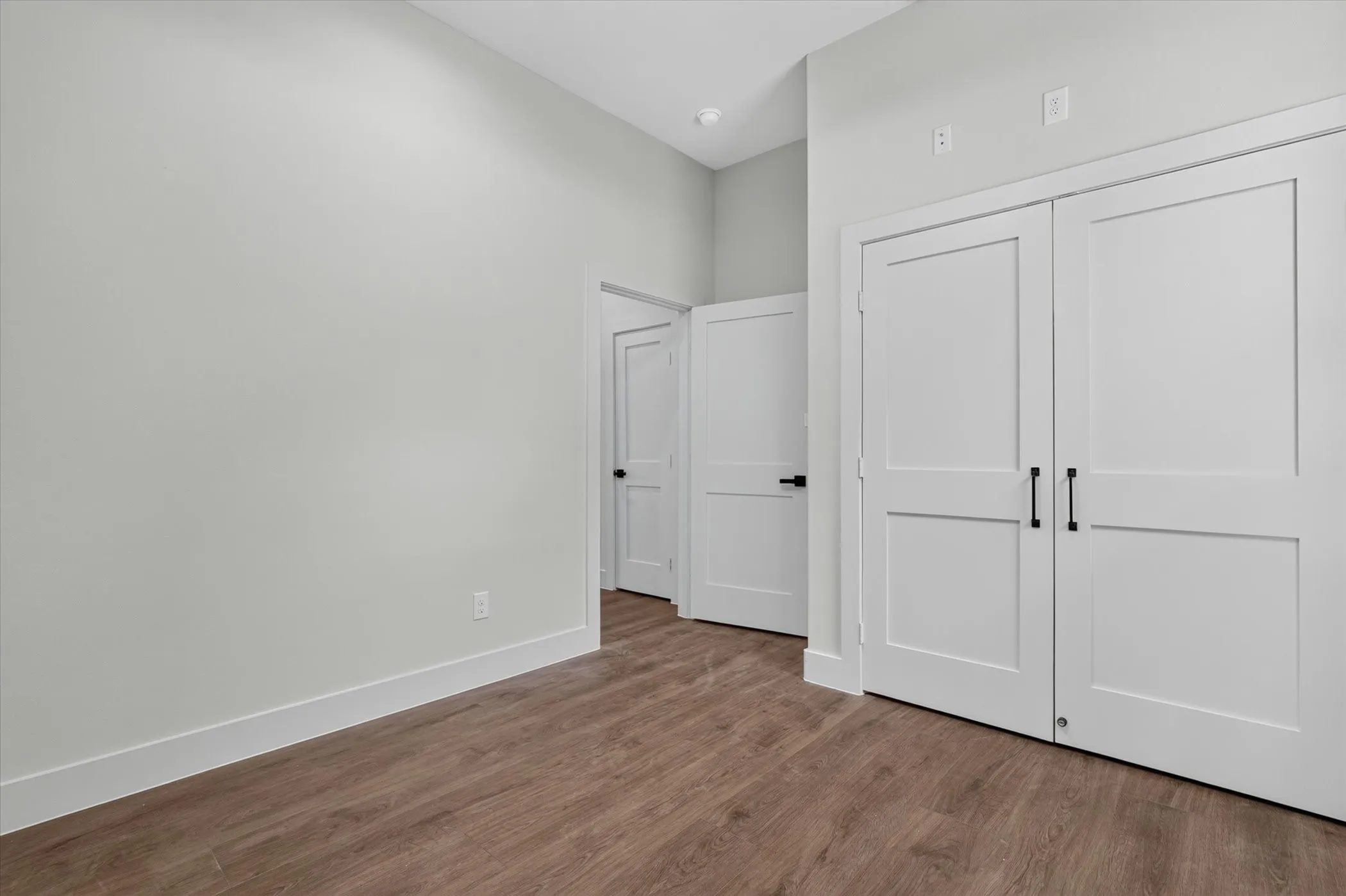 Wood-finish flooring, white flat-panel doors with matte black hardware, and crisp white trim