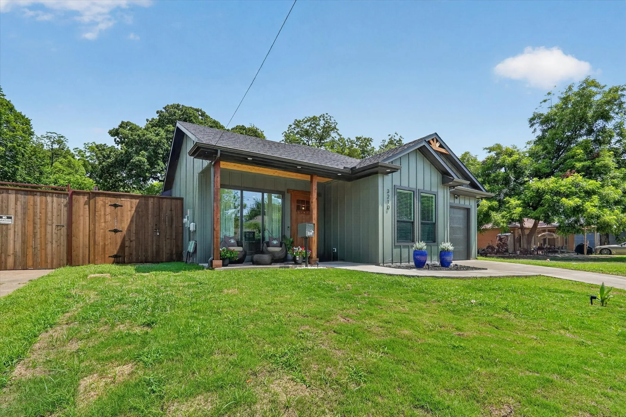 Board and batten siding, covered front porch with wood columns, attached garage, concrete driveway, and wood privacy fencing