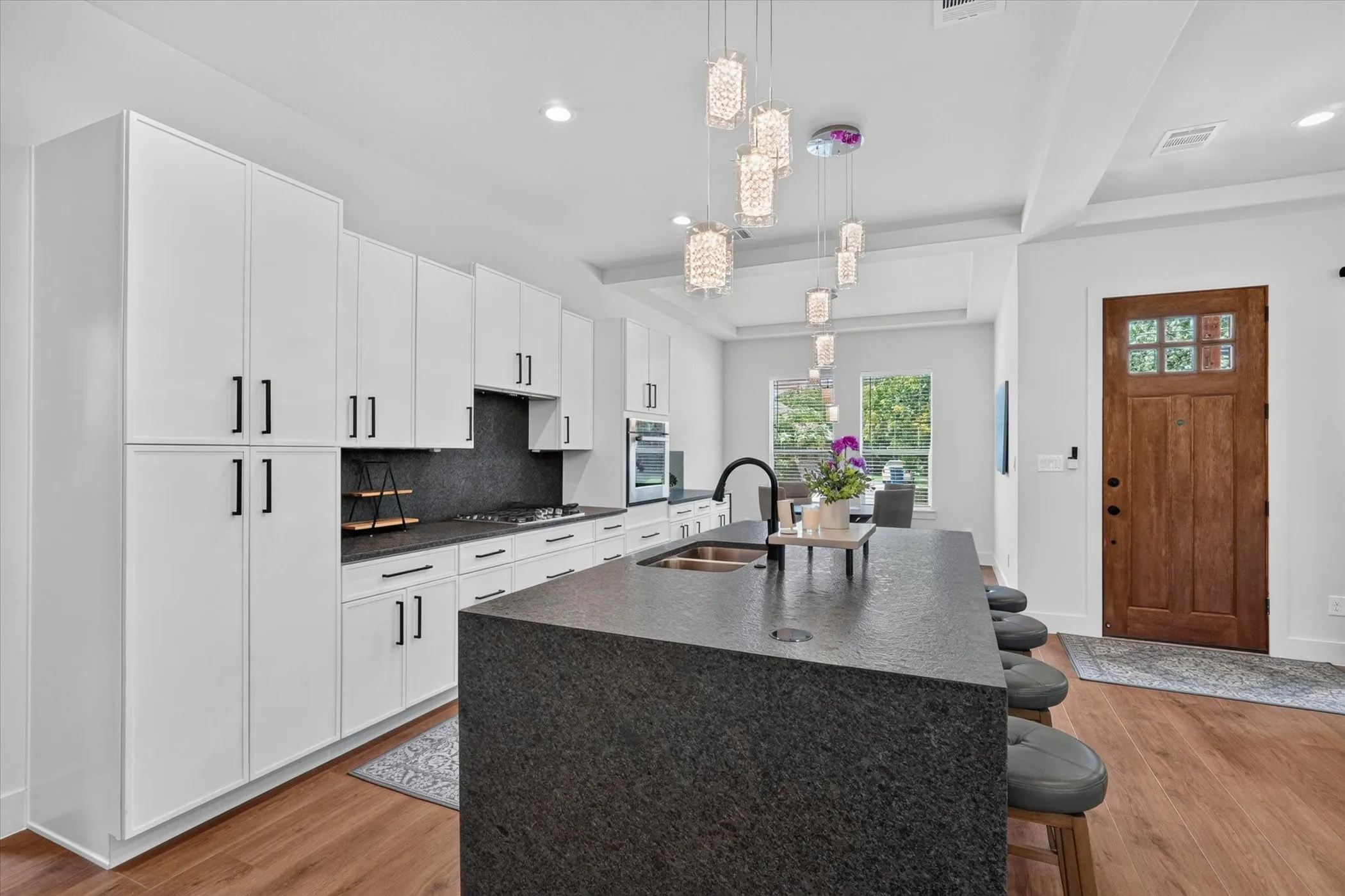 Gourmet kitchen featuring white cabinetry, a large center island with integrated sink, black stone countertops, and wood-finish flooring