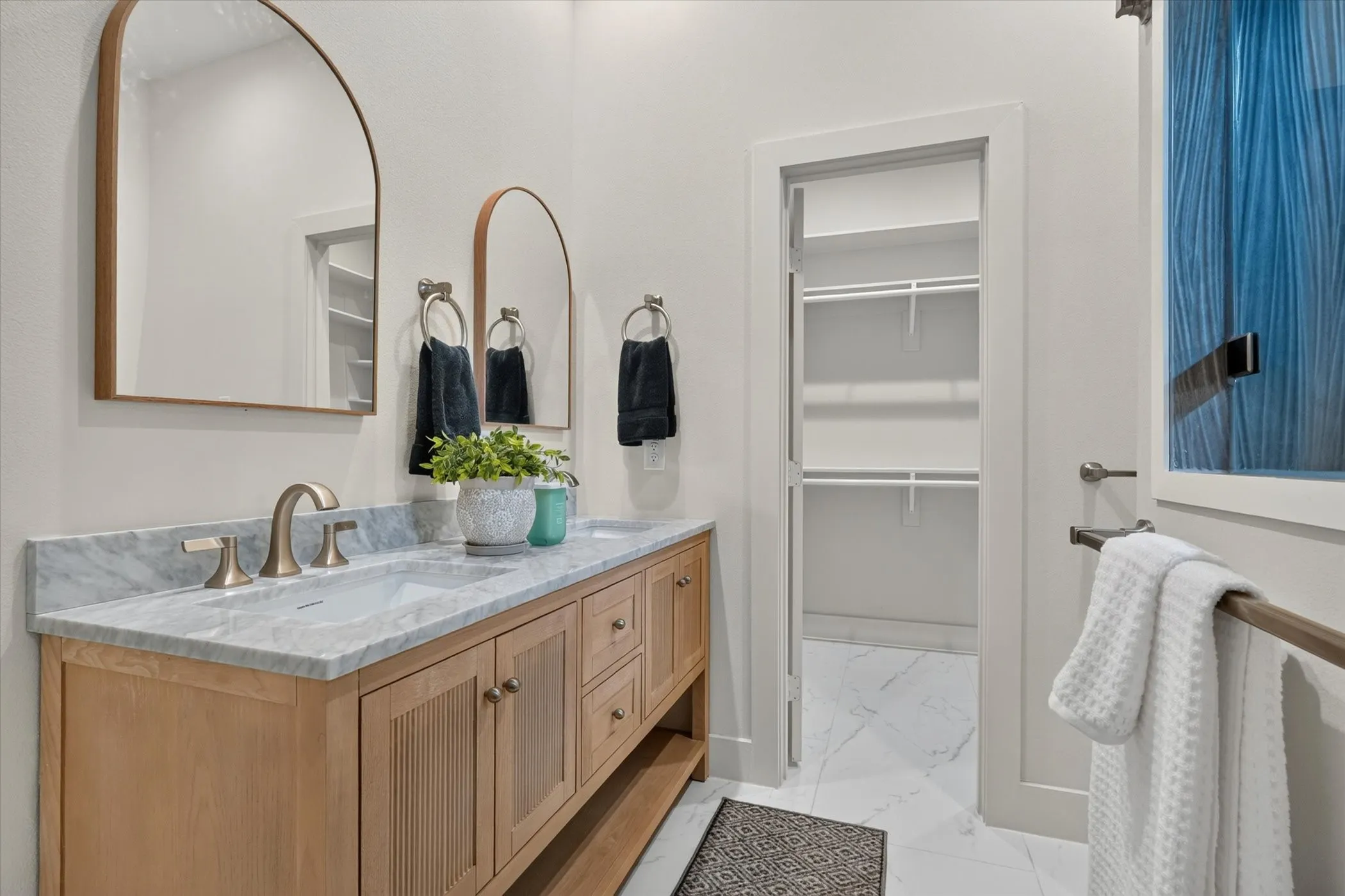 Double vanity with undermount sinks and light wood-finish cabinetry, arched mirrors, and a walk-in closet with built-in shelving