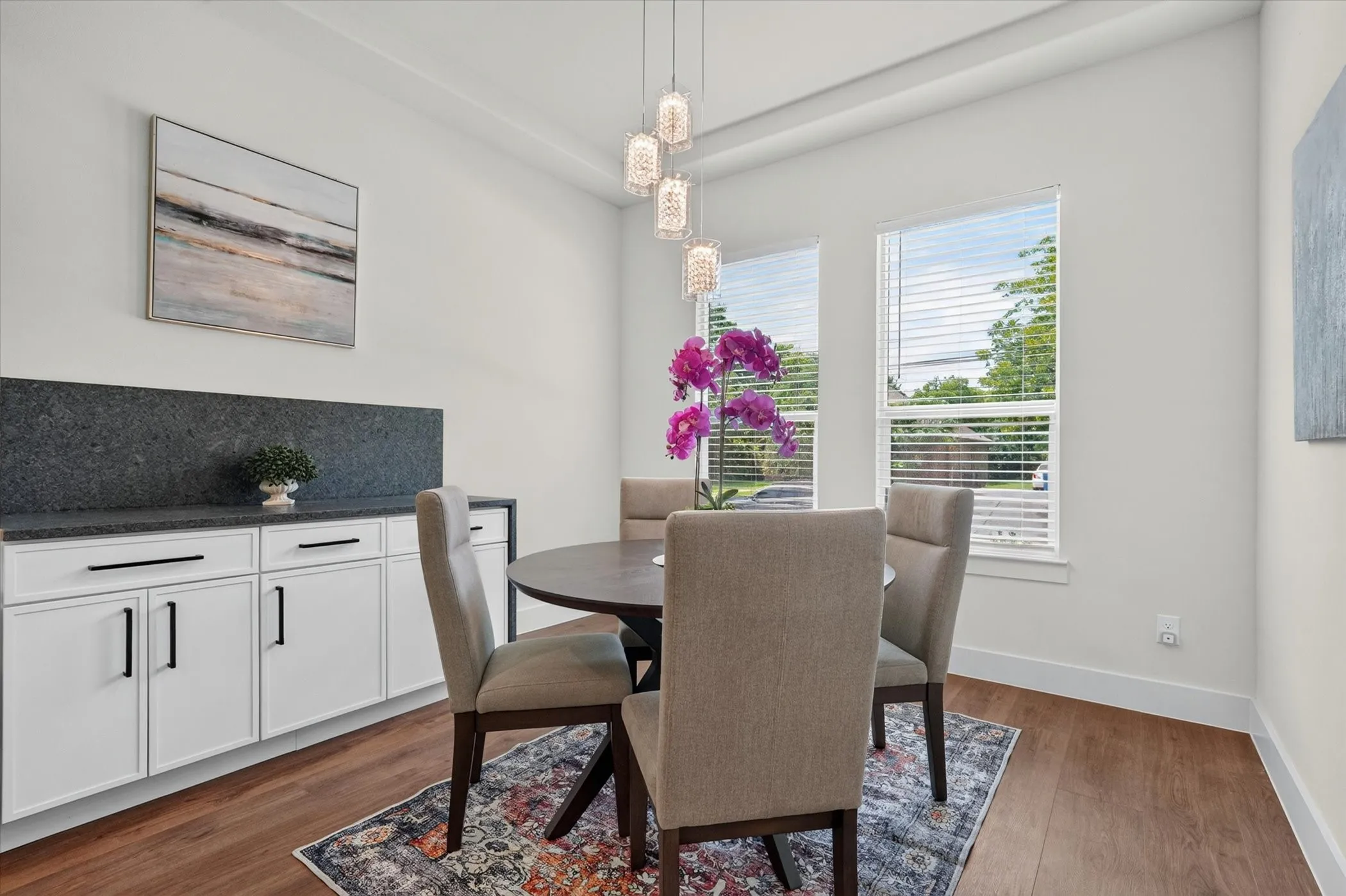 Wood-finish flooring, white cabinetry with black hardware, dark stone countertop with matching backsplash, and a contemporary chandelier