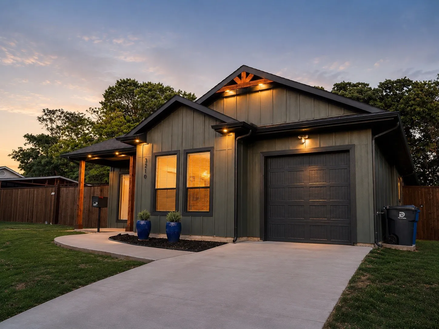 Board and batten exterior with contrasting trim, attached garage, concrete driveway, covered entry, and wood privacy fencing