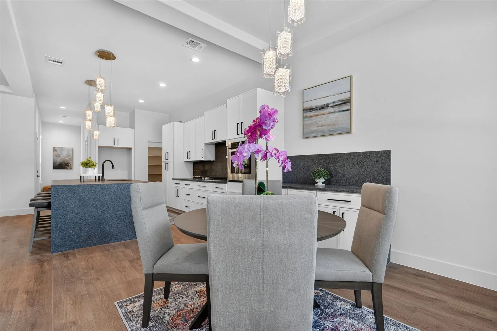 White cabinetry with dark hardware, recessed lighting, wood-finish flooring, dark textured kitchen island, and contemporary light fixtures