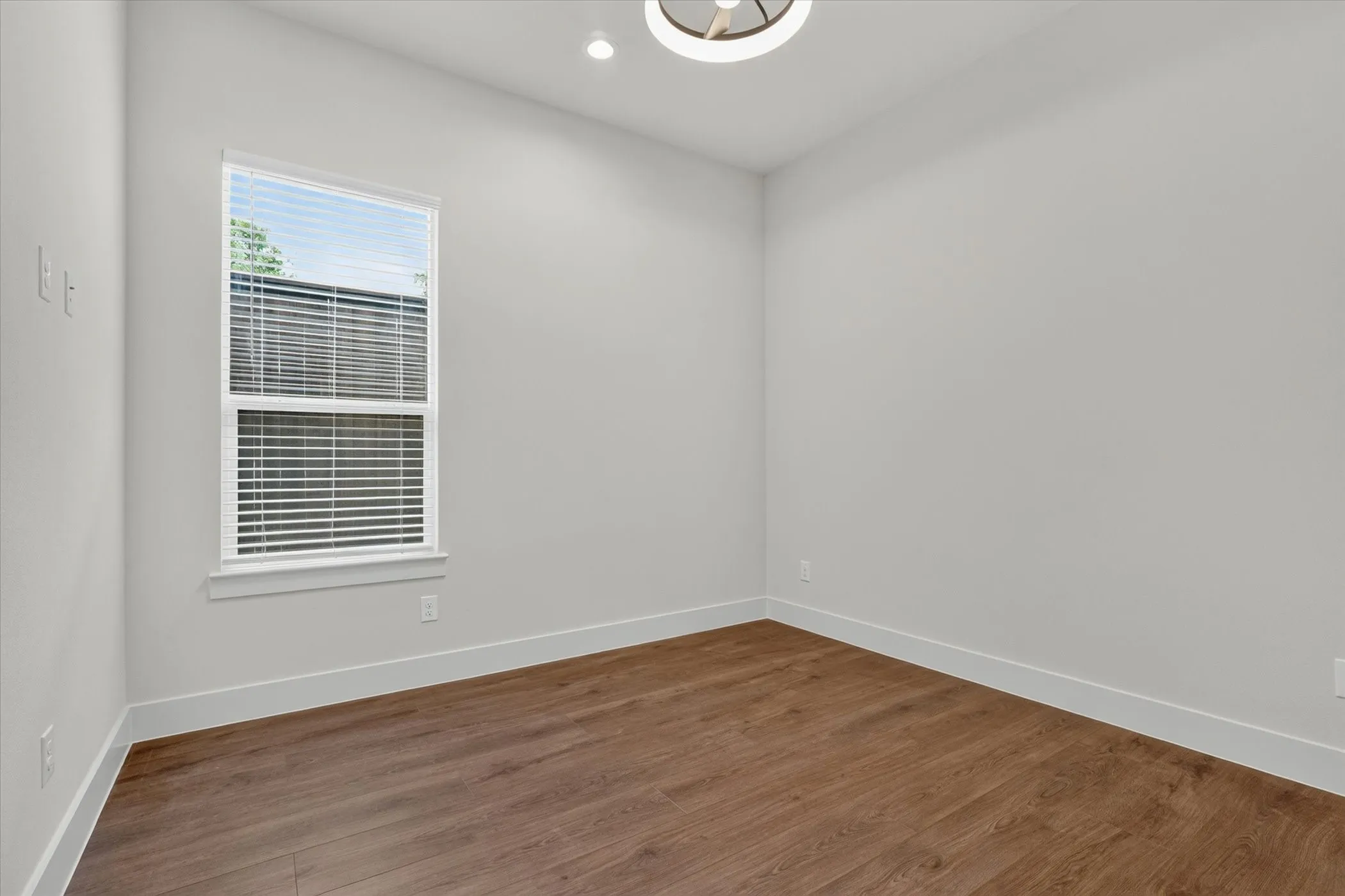 Wood-finish flooring, white trim, single window with blinds, recessed lighting, and a contemporary ceiling fixture