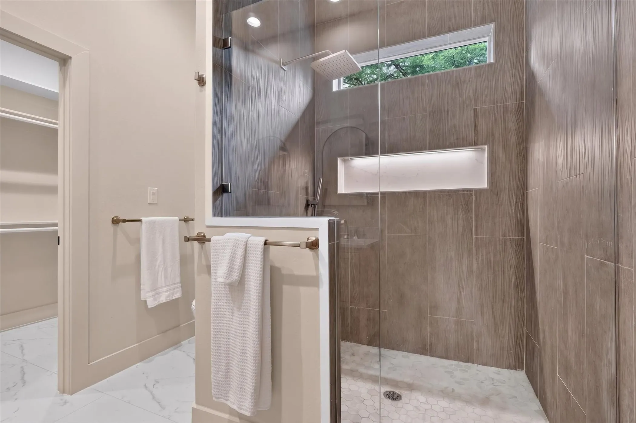 Glass-enclosed shower with a rainfall showerhead, tiled walls, and an illuminated recessed niche