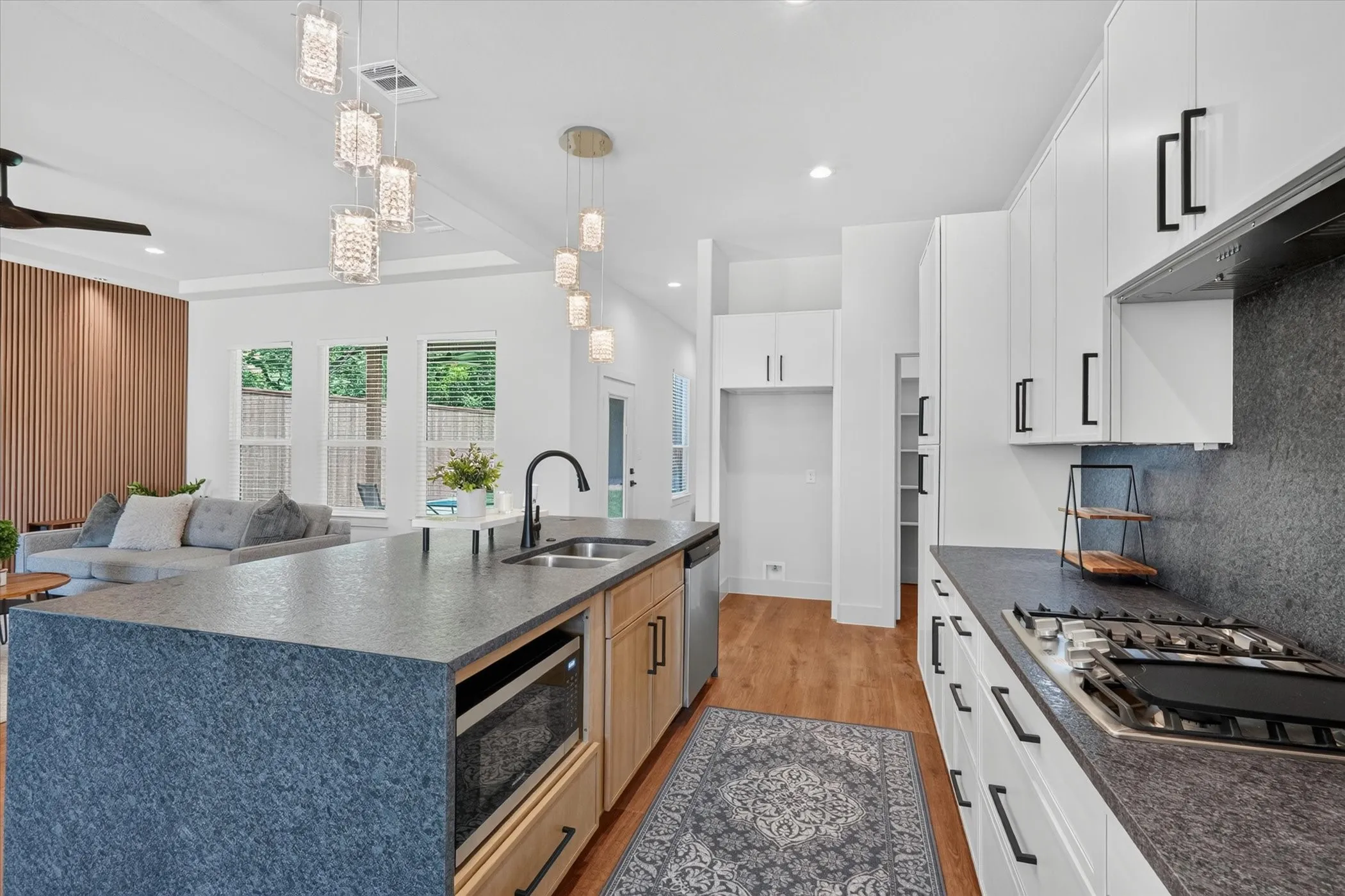 Spacious kitchen featuring an expansive island with an undermount sink, gas range, built-in microwave, and wood-finish flooring