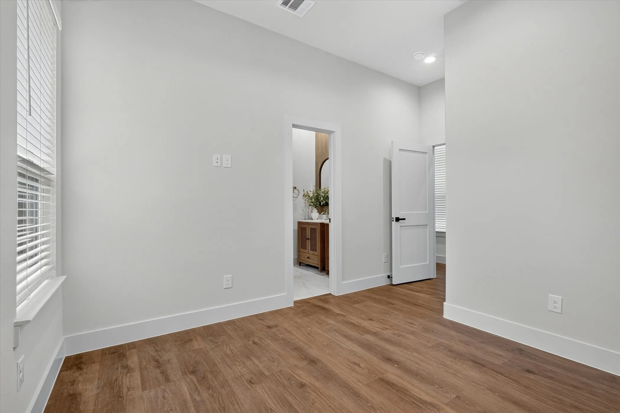Wood-finish flooring with white baseboards, recessed lighting, and a window with blinds