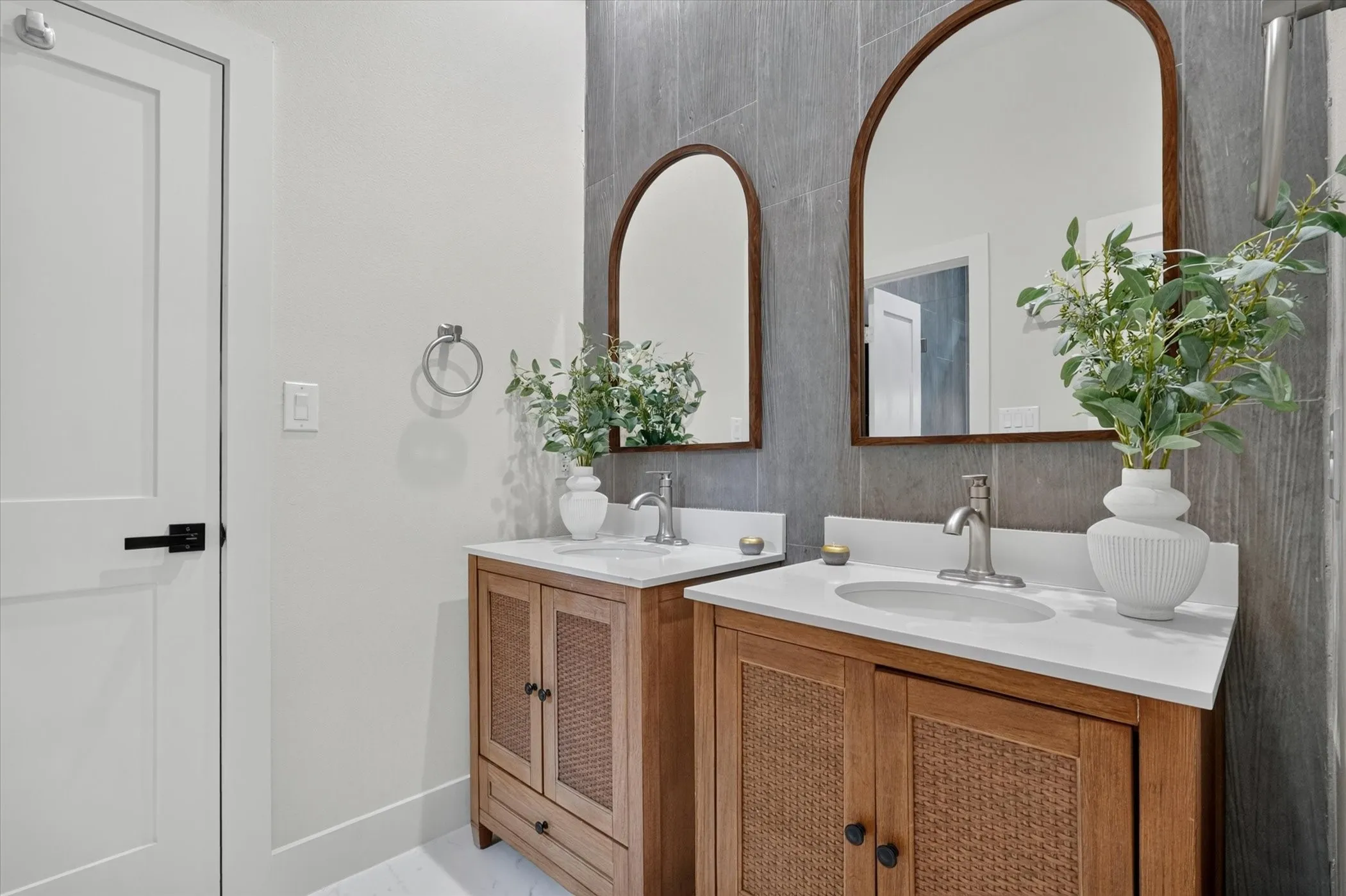 Dual wood-finish vanities with woven cane door panels, white countertops, and integrated sinks