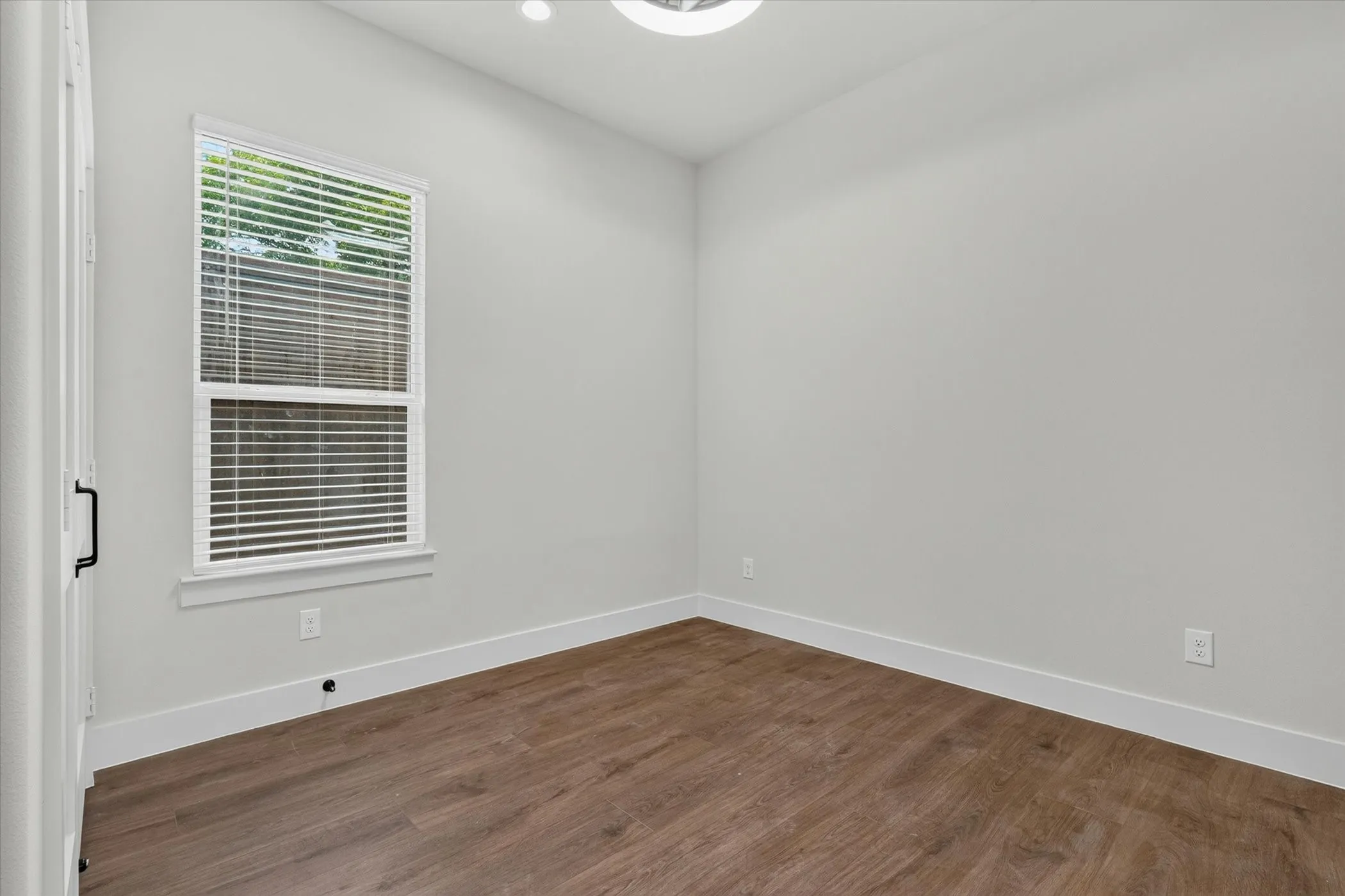 Wood-finish flooring, white walls, recessed lighting, and a window with blinds