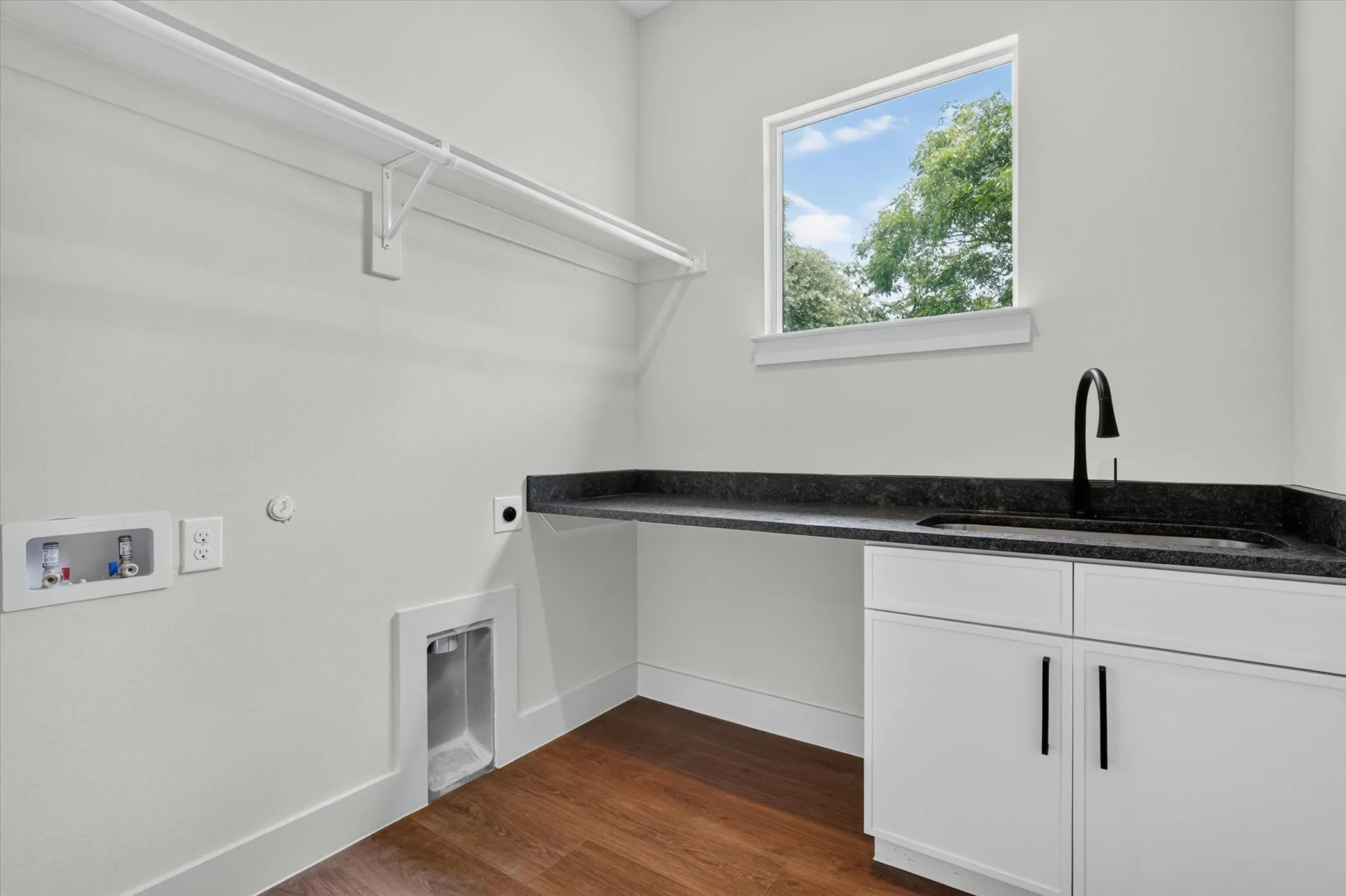 Built-in cabinetry with dark hardware, dark countertop with an integrated sink, and wood-finish flooring