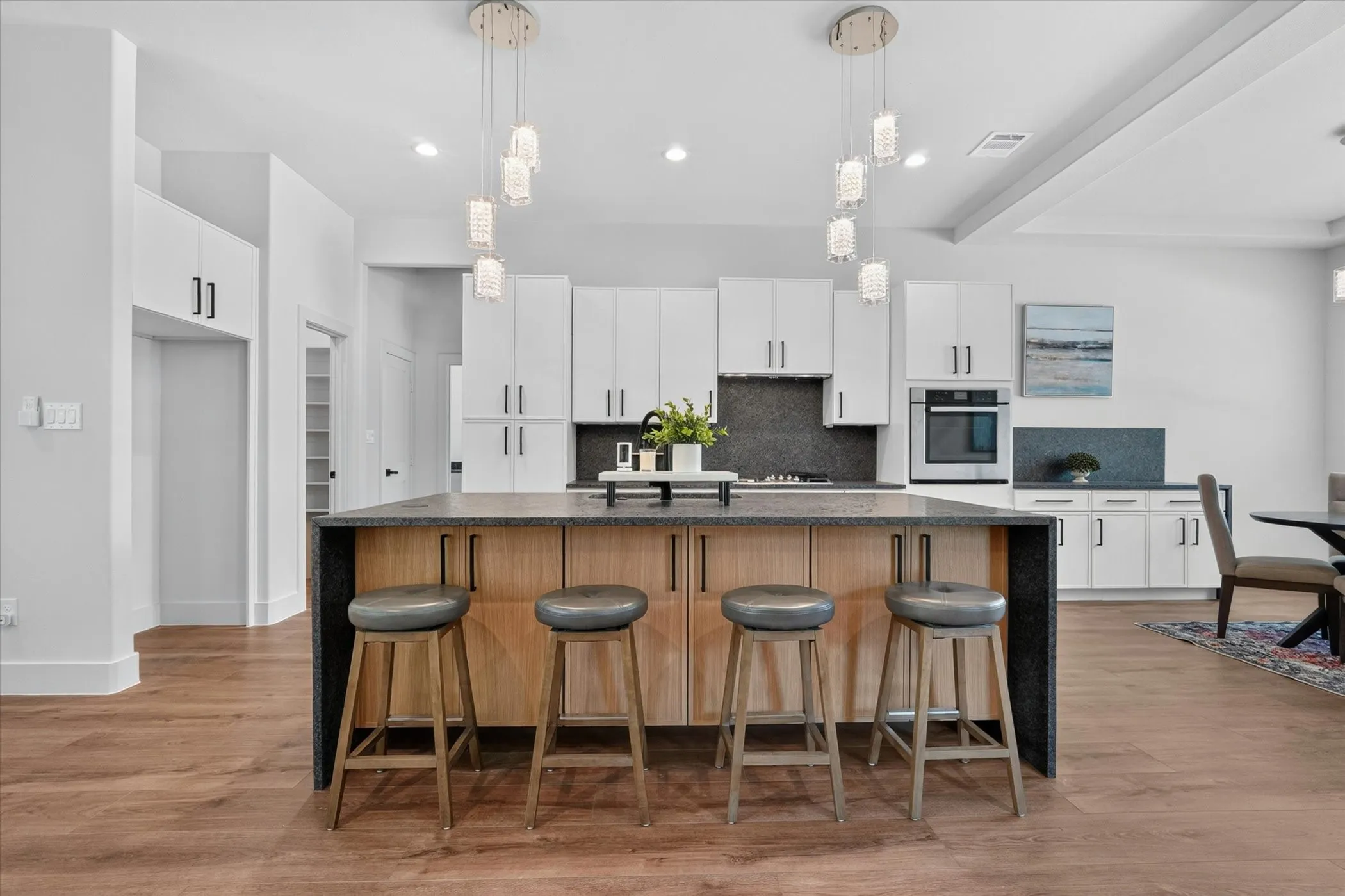 Kitchen featuring a two-tone island with dark countertops, white cabinetry with dark hardware, a built-in oven, and wood-finish flooring