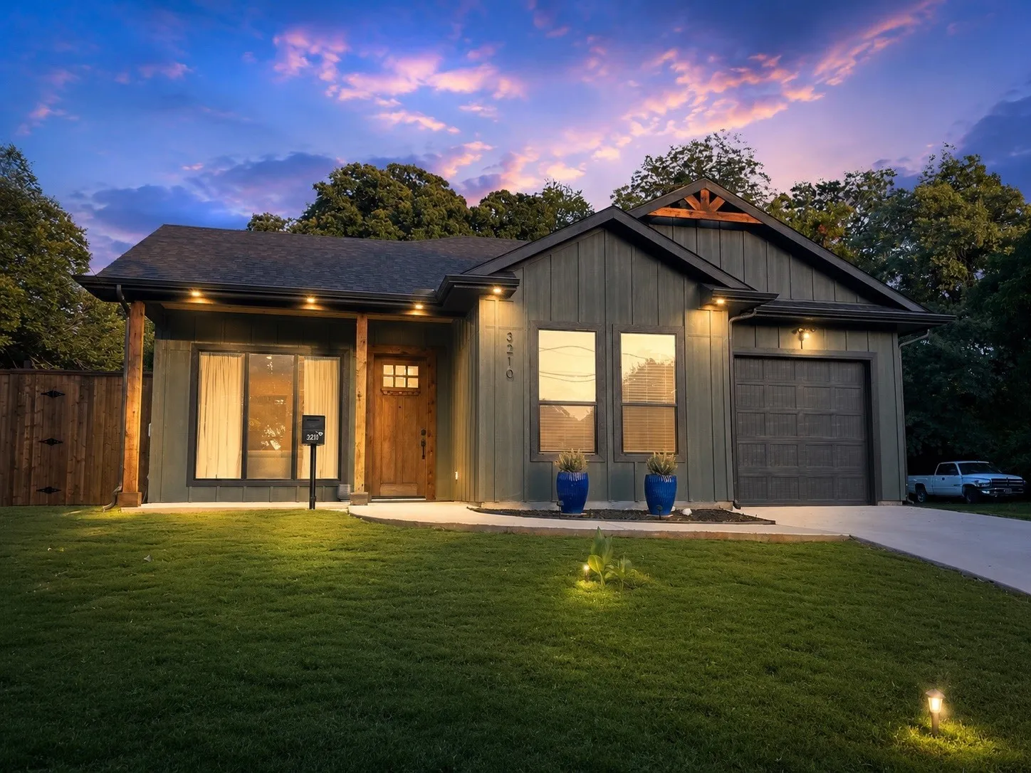 Contemporary exterior with board and batten siding, a dark asphalt shingle roof, wood-finish columns, a wood-finish front door, and an attached garage with a dark panel door