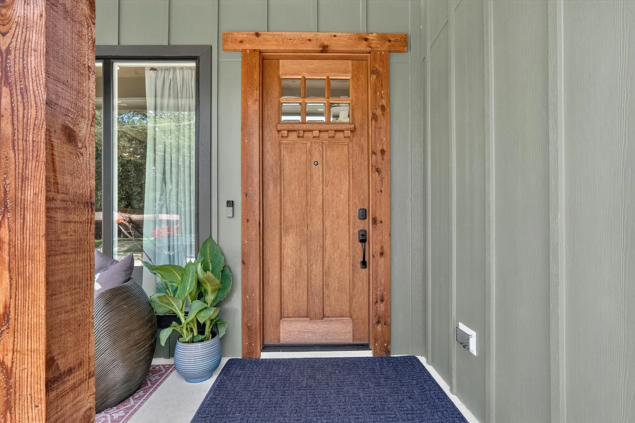 Craftsman-style wood entry door with glass paneling, board and batten siding, and a prominent wood structural beam