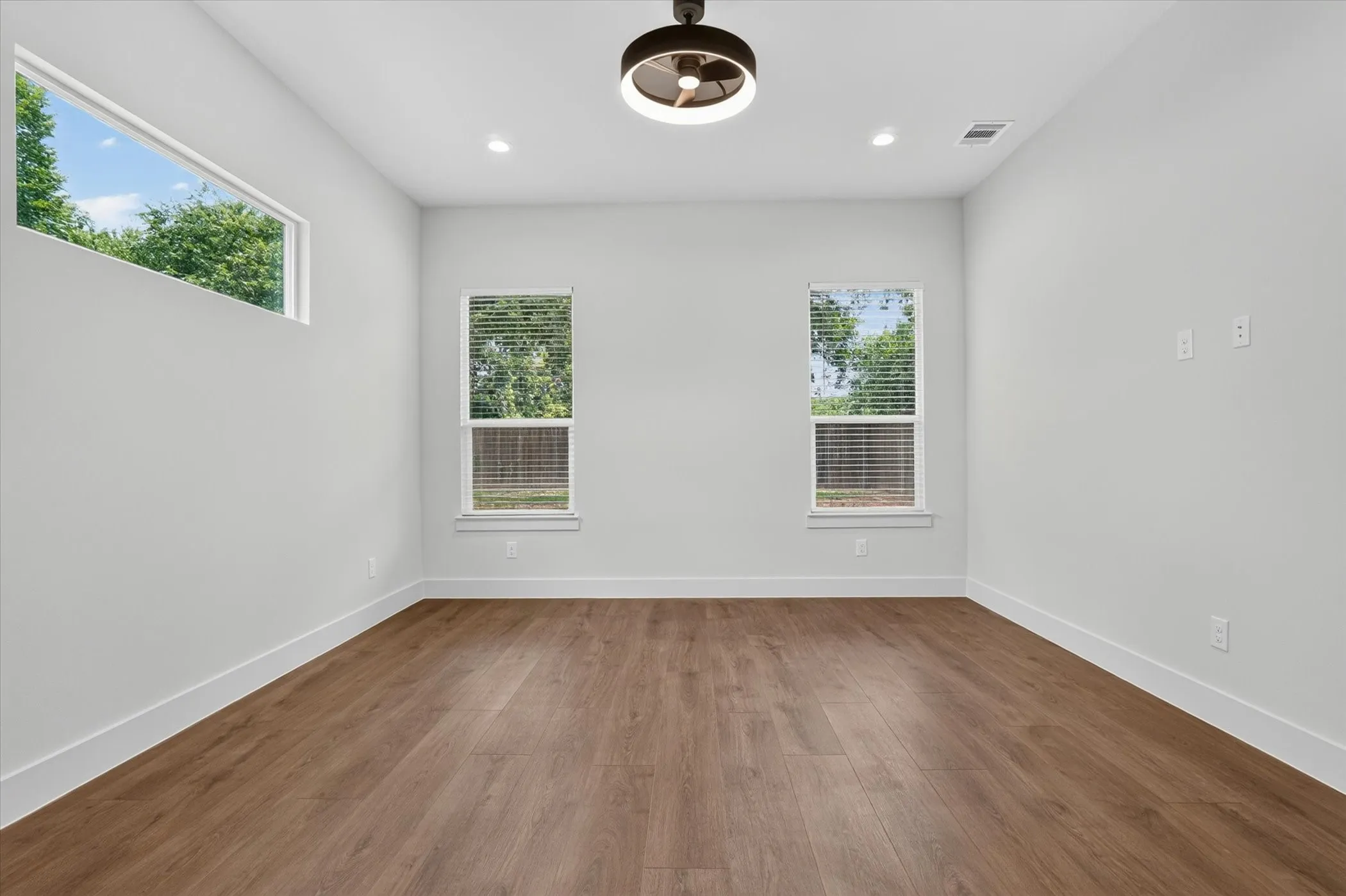 Wood-finish flooring, recessed lighting, modern ceiling fan, three windows, white walls