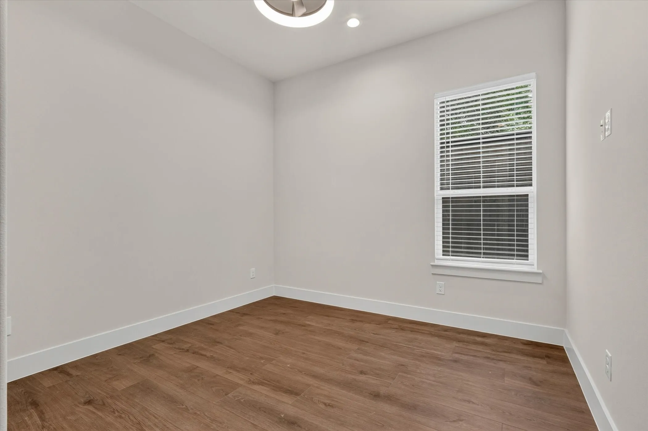 Wood-finish flooring, single window with blinds, ceiling-mounted light fixture, white trim